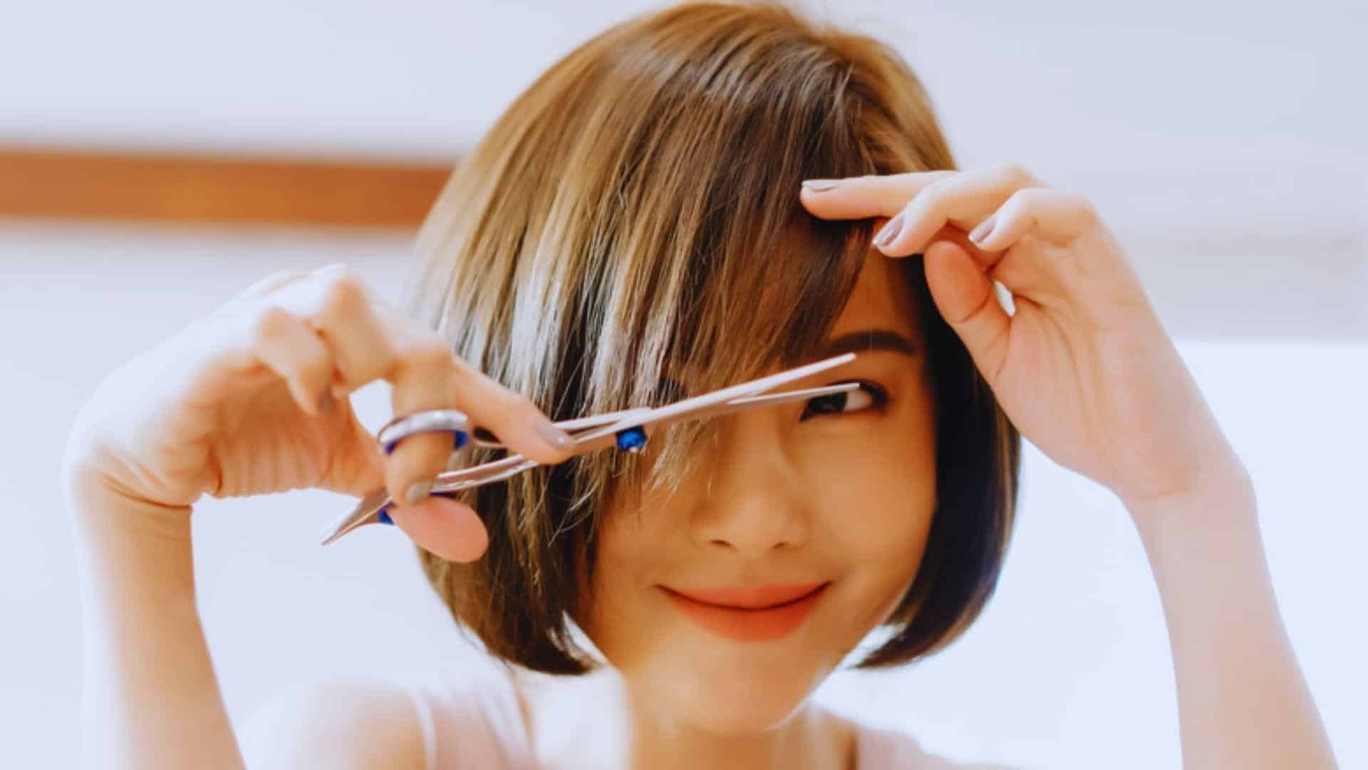 A woman is trimming her hair with scissors, demonstrating a careful and deliberate approach.