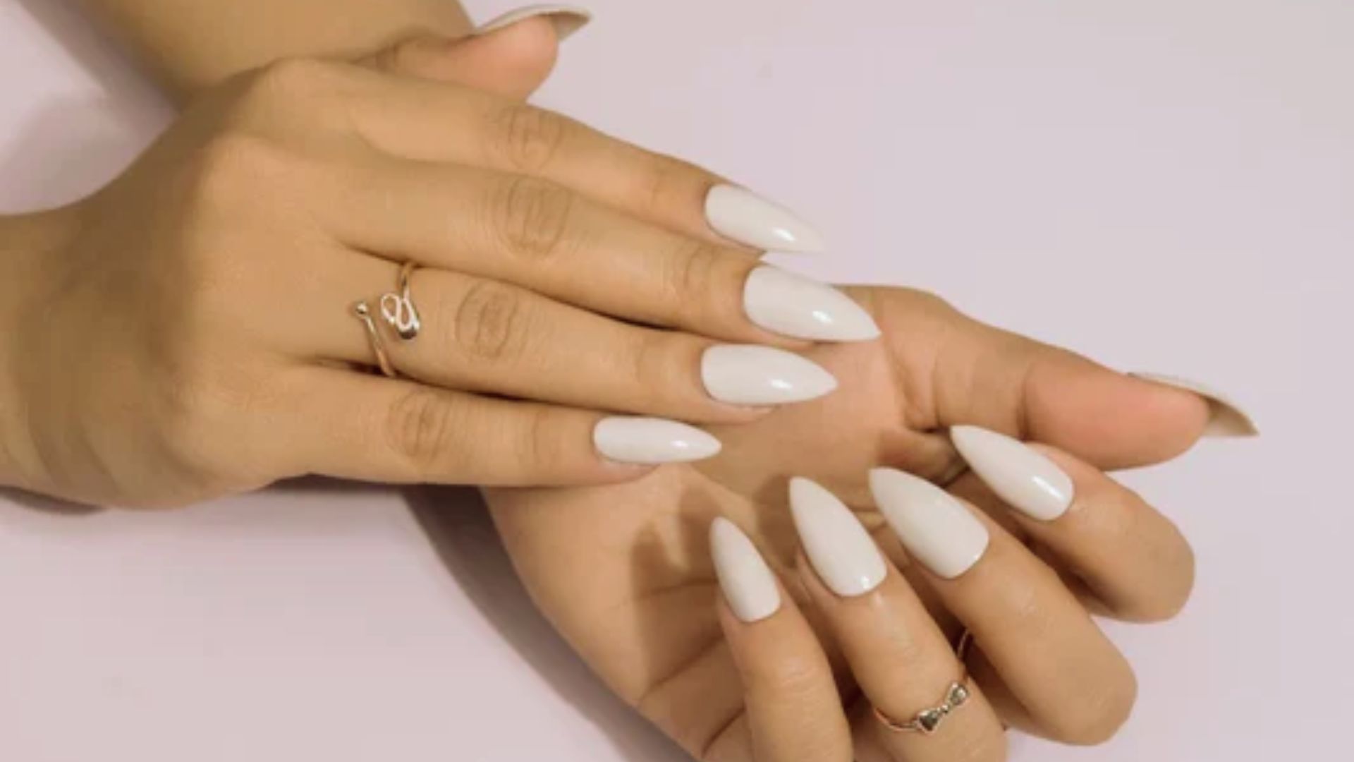 A close-up of a woman's hands with white nails adorned with multiple rings, showcasing elegance and style.