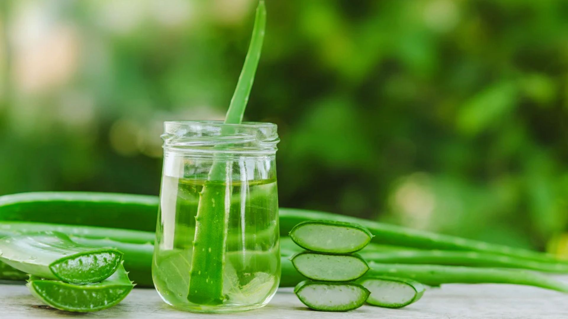Aloe vera juice in a glass beside fresh aloe vera leaves on a rustic wooden table.