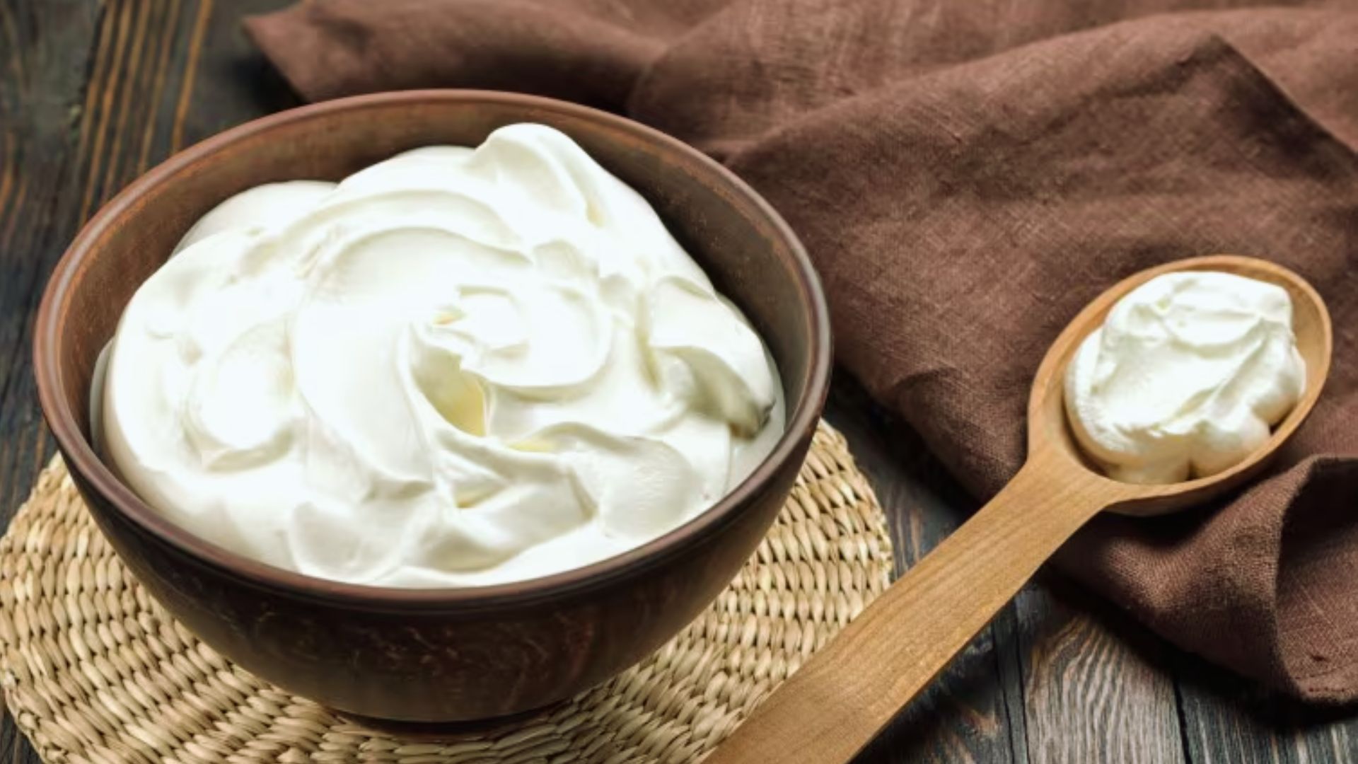 A bowl of yogurt with a spoon rests on a wooden table, showcasing a simple and inviting breakfast setting.