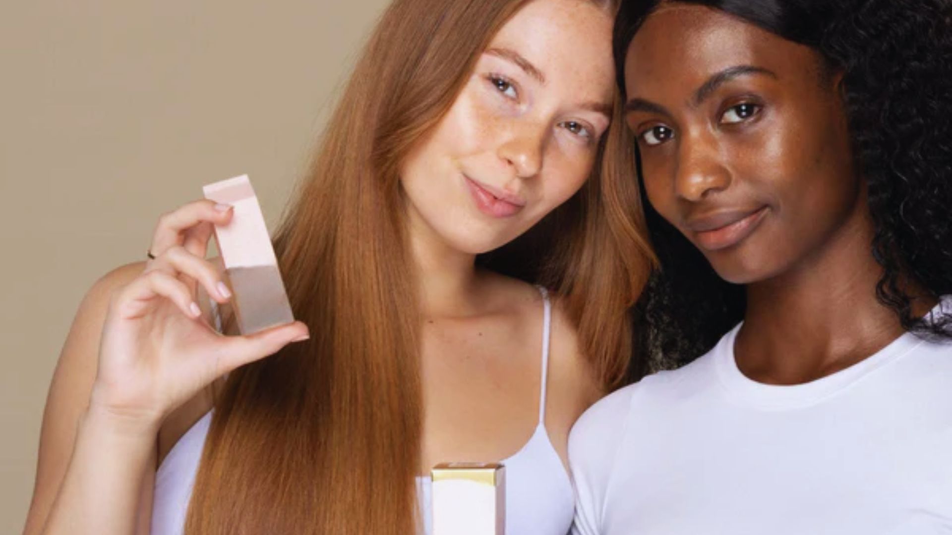 Two women smiling while holding a makeup product, showcasing its features and promoting its use.