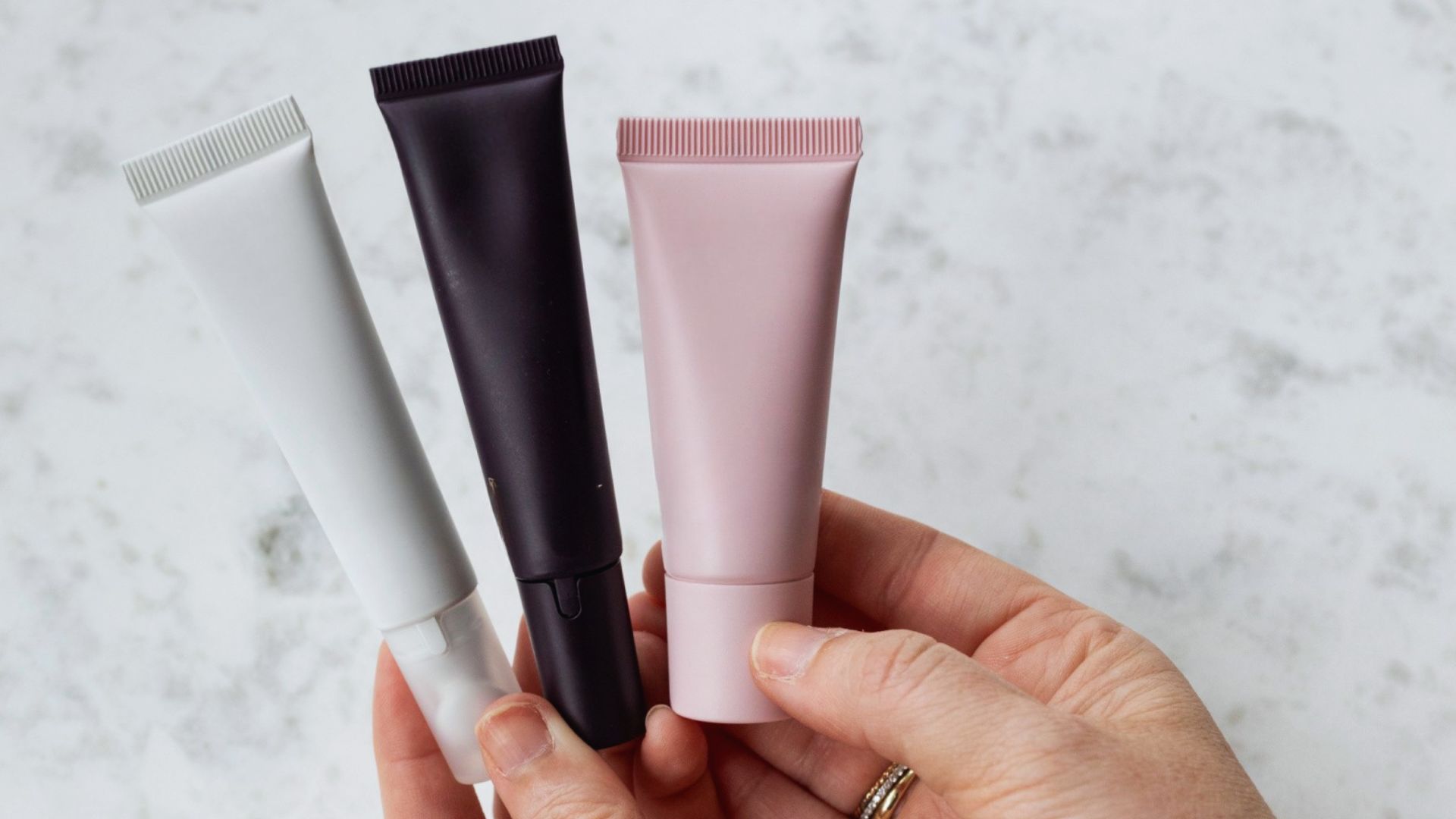 A hand holding three tubes of cream, showcasing various sizes and colors of the packaging.