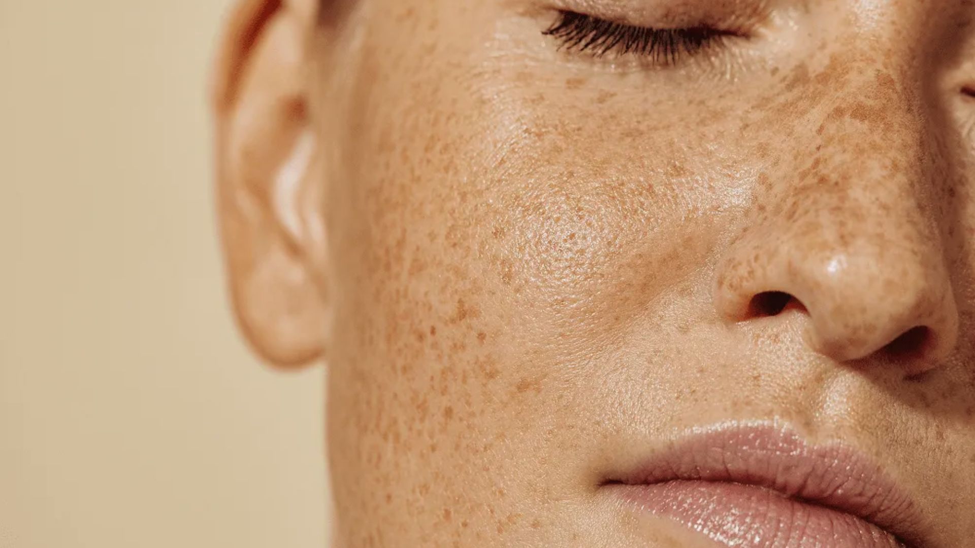A woman with freckles on her face smiles softly, showcasing her natural beauty and warm expression.