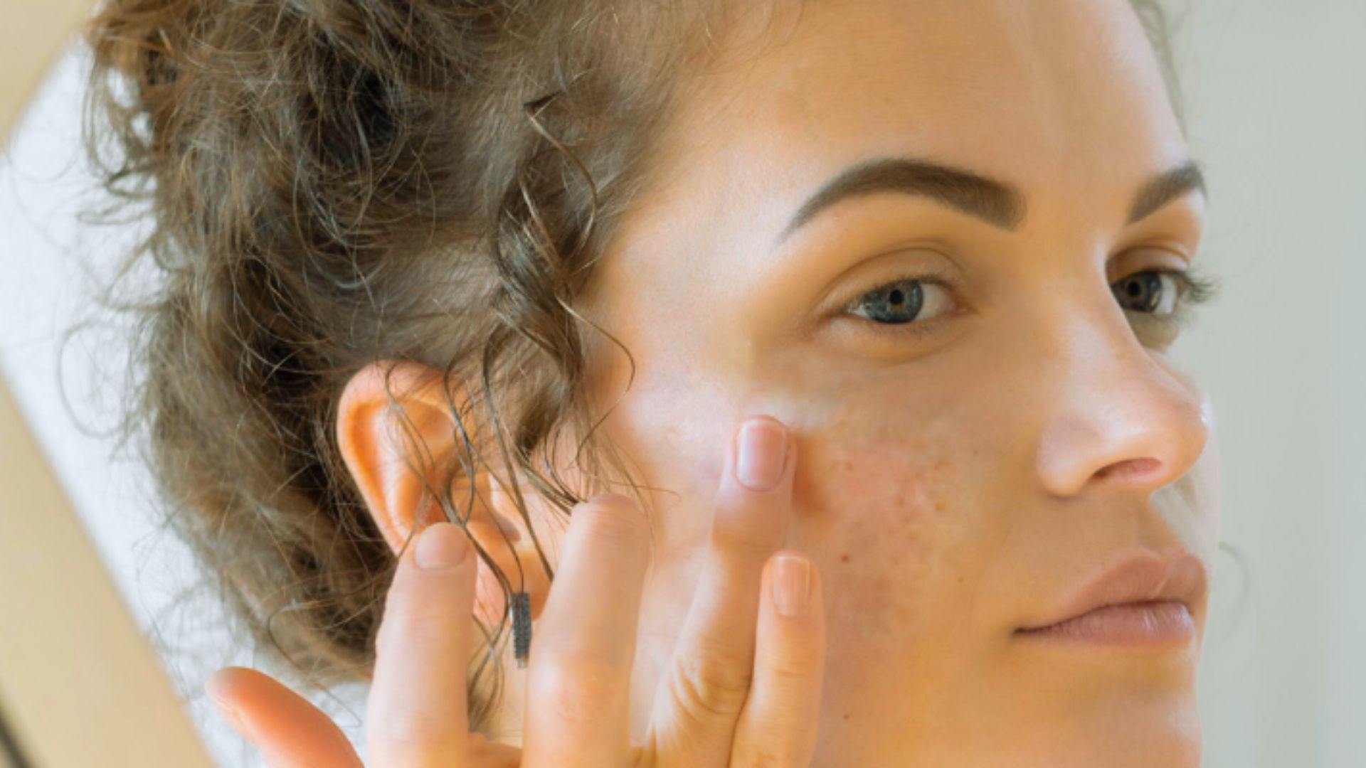 A woman gazes at her reflection in a mirror, examining her face with a thoughtful expression.