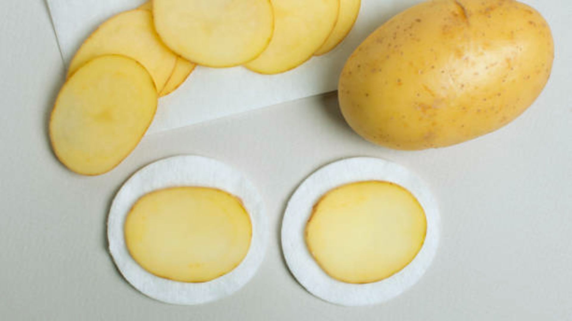 A potato sliced in half, revealing its interior, accompanied by two additional potato slices beside it.