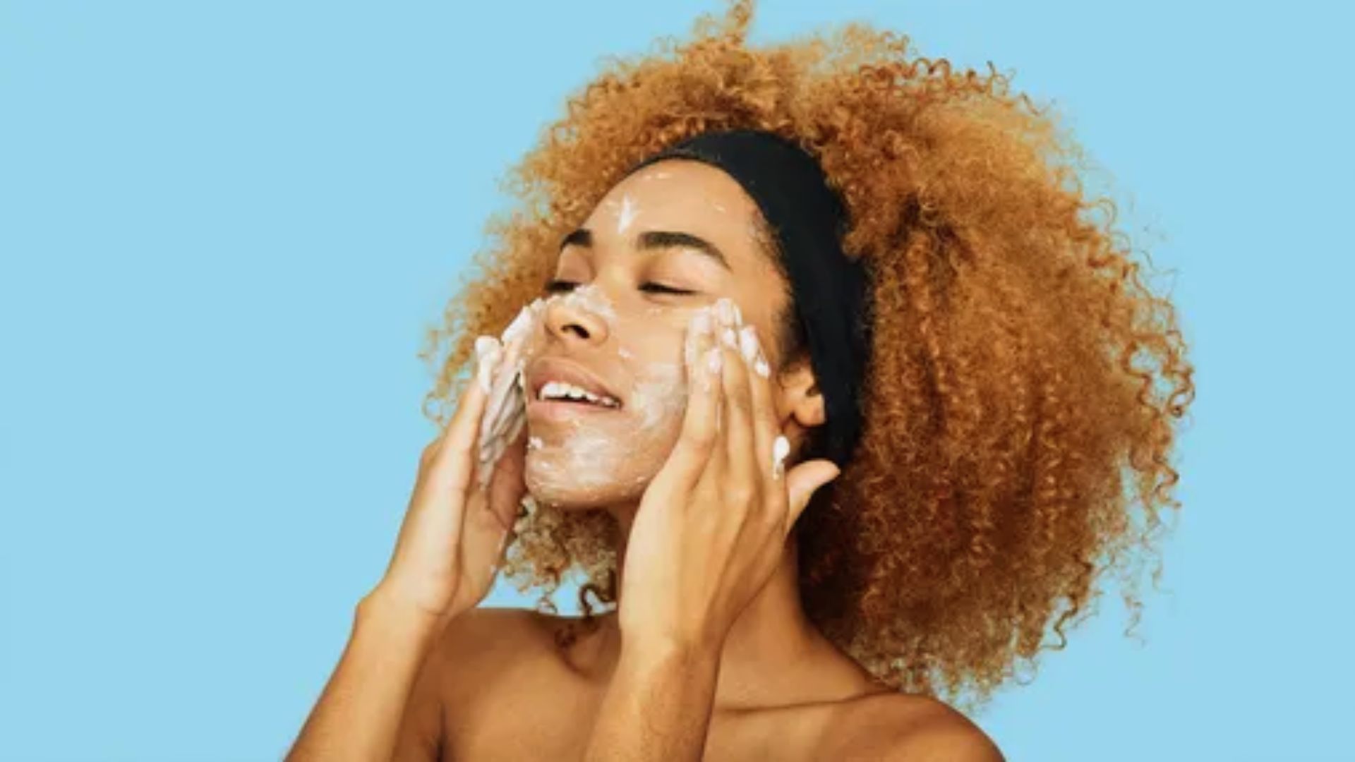 A woman with curly hair wearing a face mask, looking directly at the camera with a neutral expression.