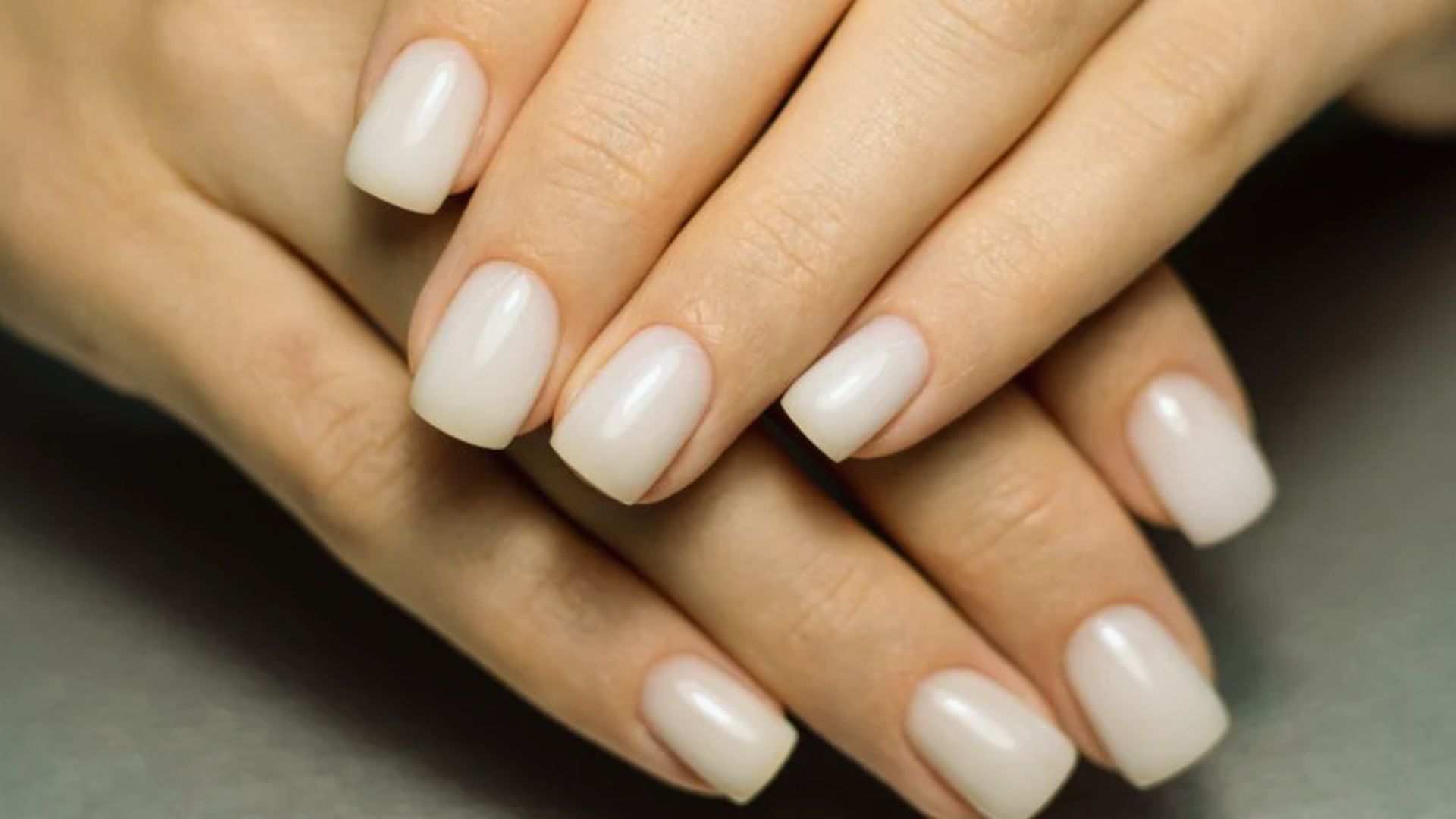 A close-up of a woman's hands with neatly manicured white nails resting on a surface.