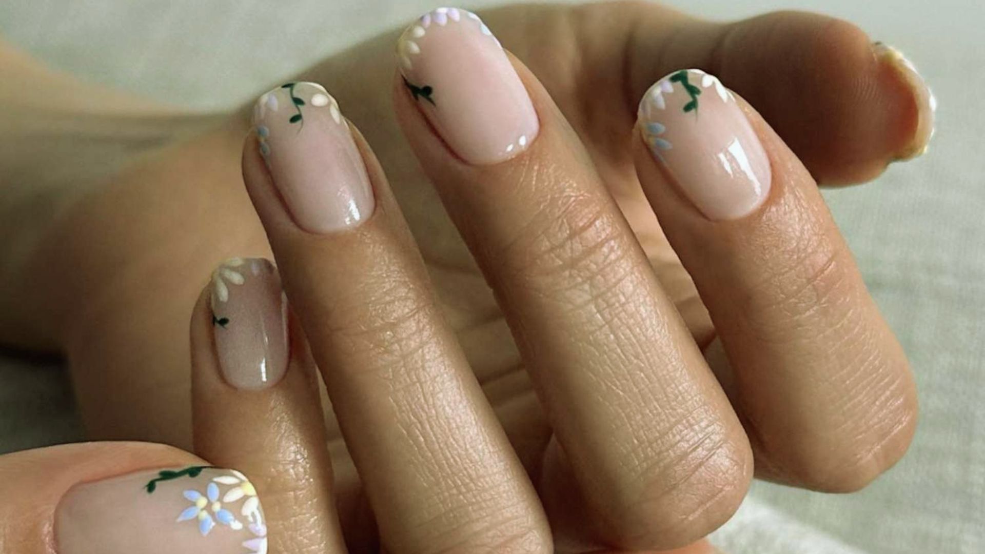 A woman with long nails showcases a white and pink manicure, highlighting her elegant hand gesture.