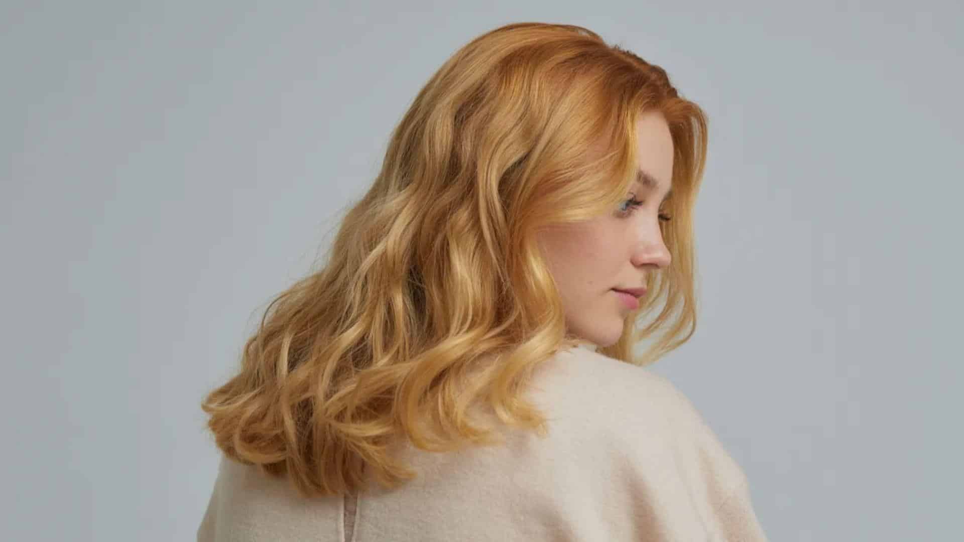 A woman with long red hair gazes away from the camera, her profile highlighted against a soft background.