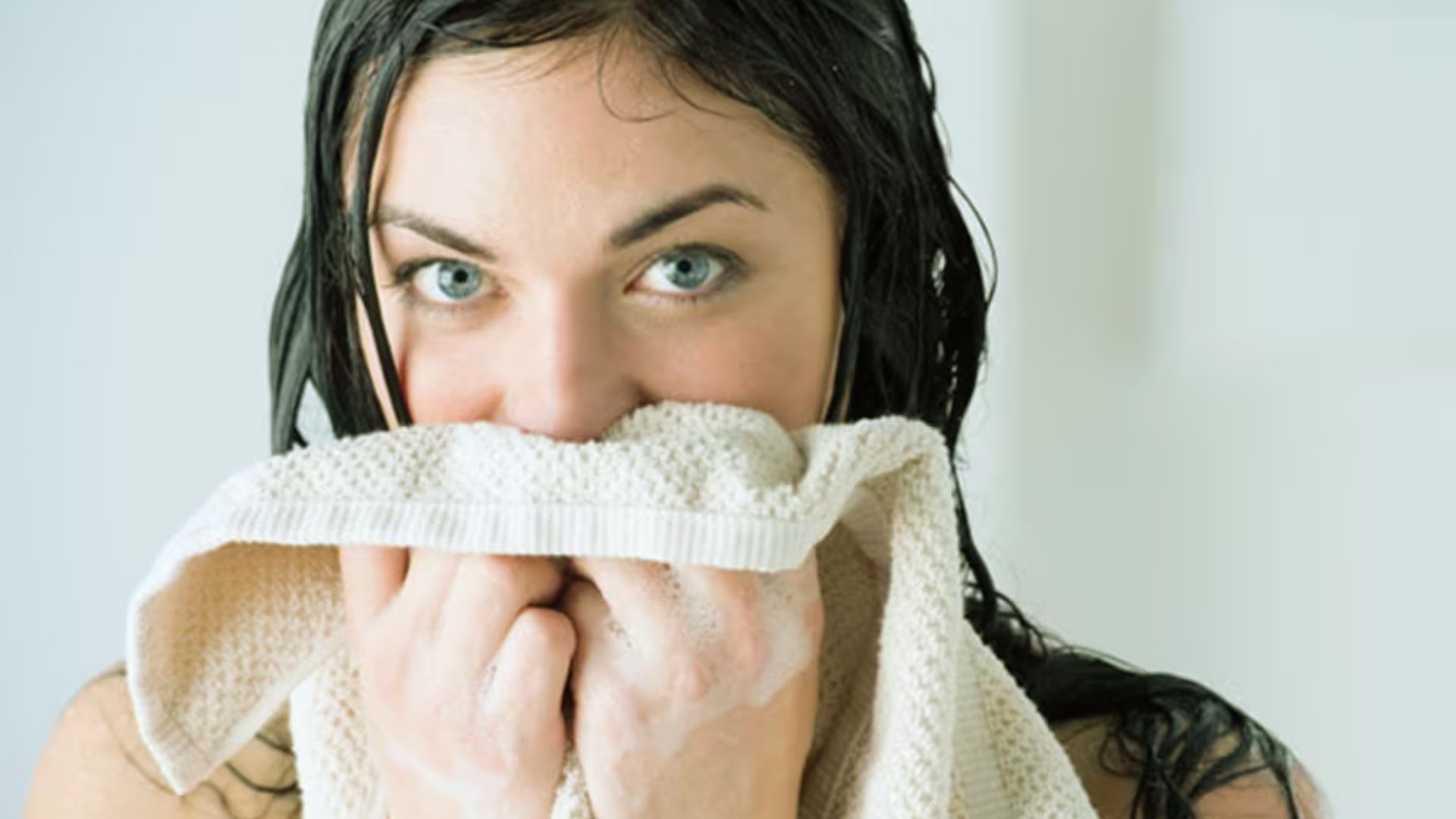 A woman holds a towel to her face, possibly drying off or soothing her skin after a wash or workout.