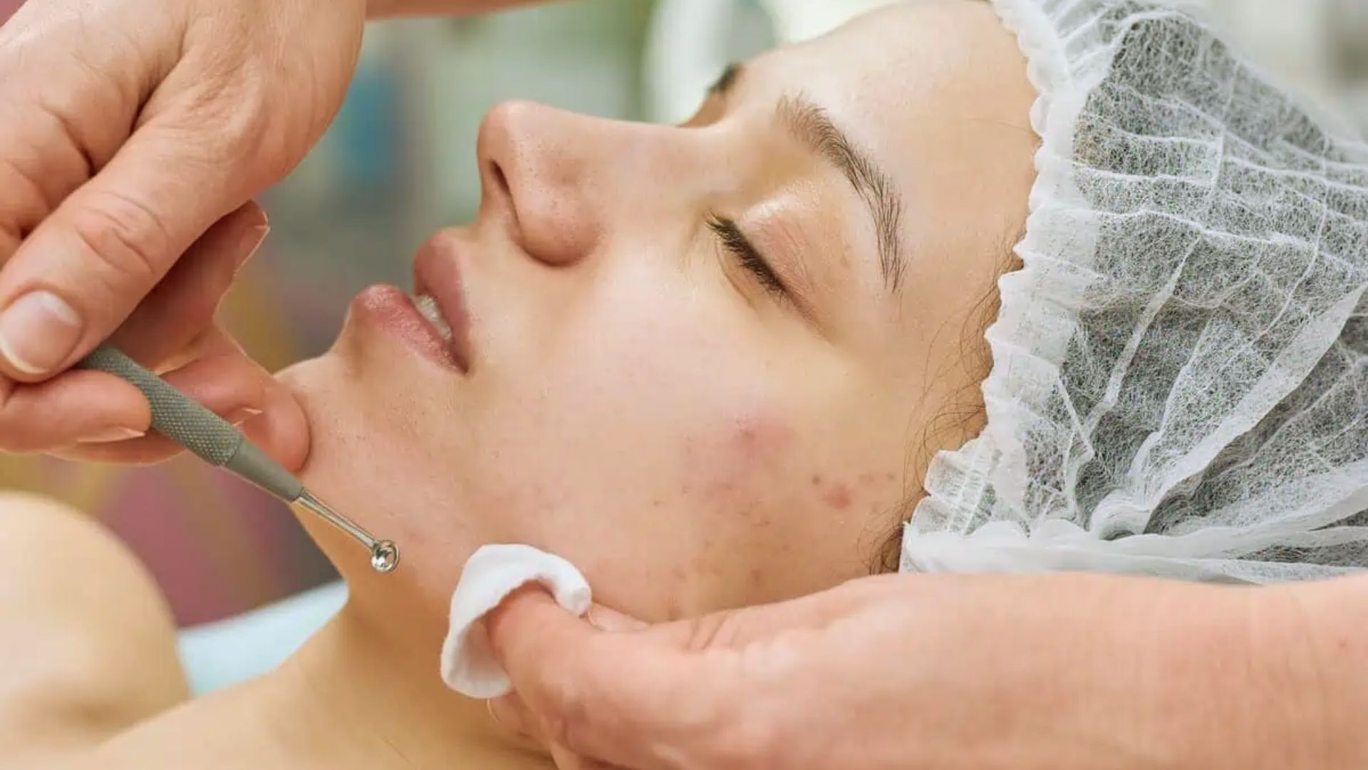 A woman receiving a facial treatment, relaxing on a spa bed with a serene expression and a therapist applying products.