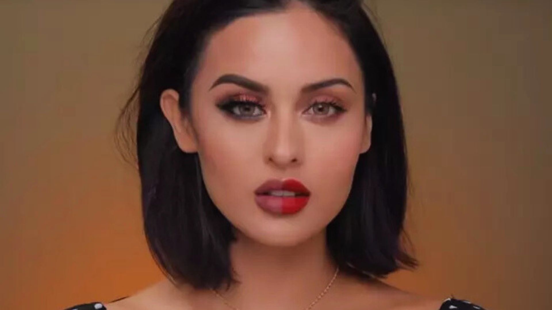 A woman wearing a black top and red lipstick, showcasing a confident expression.
