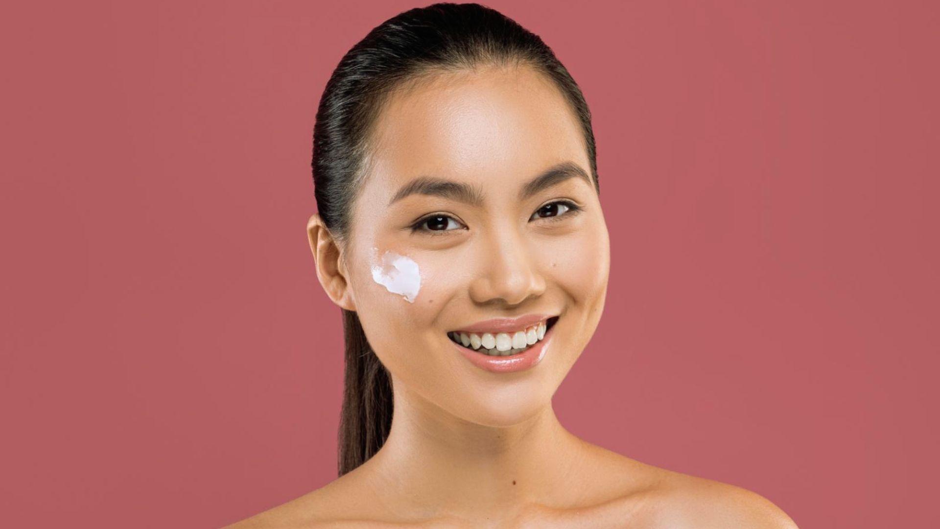 A woman smiling with cream applied to her face, showcasing a joyful expression and skincare routine.