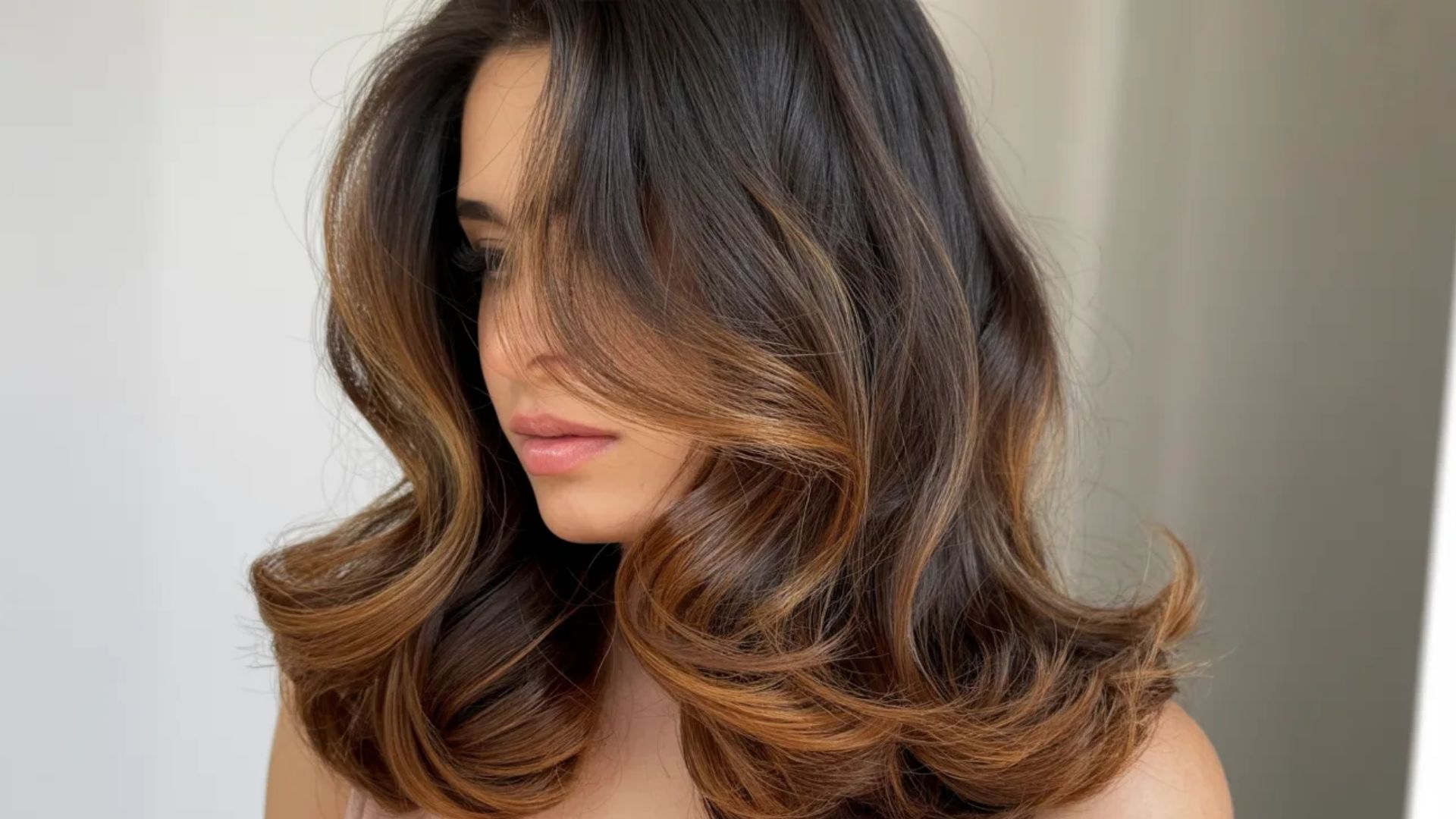 A woman with long, wavy hair featuring brown highlights cascading down her shoulders.