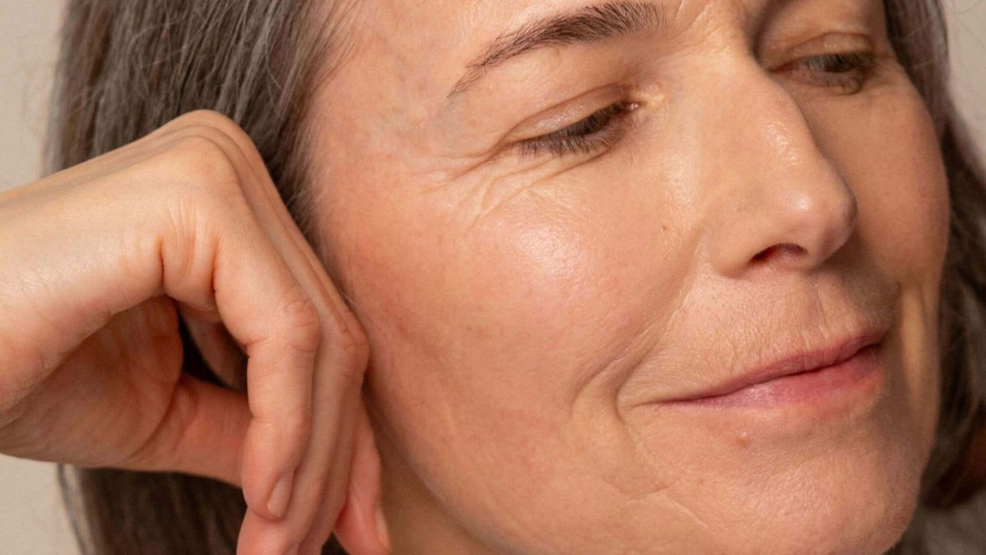 A woman with facial wrinkles gently touches her ear, conveying a moment of contemplation or listening.