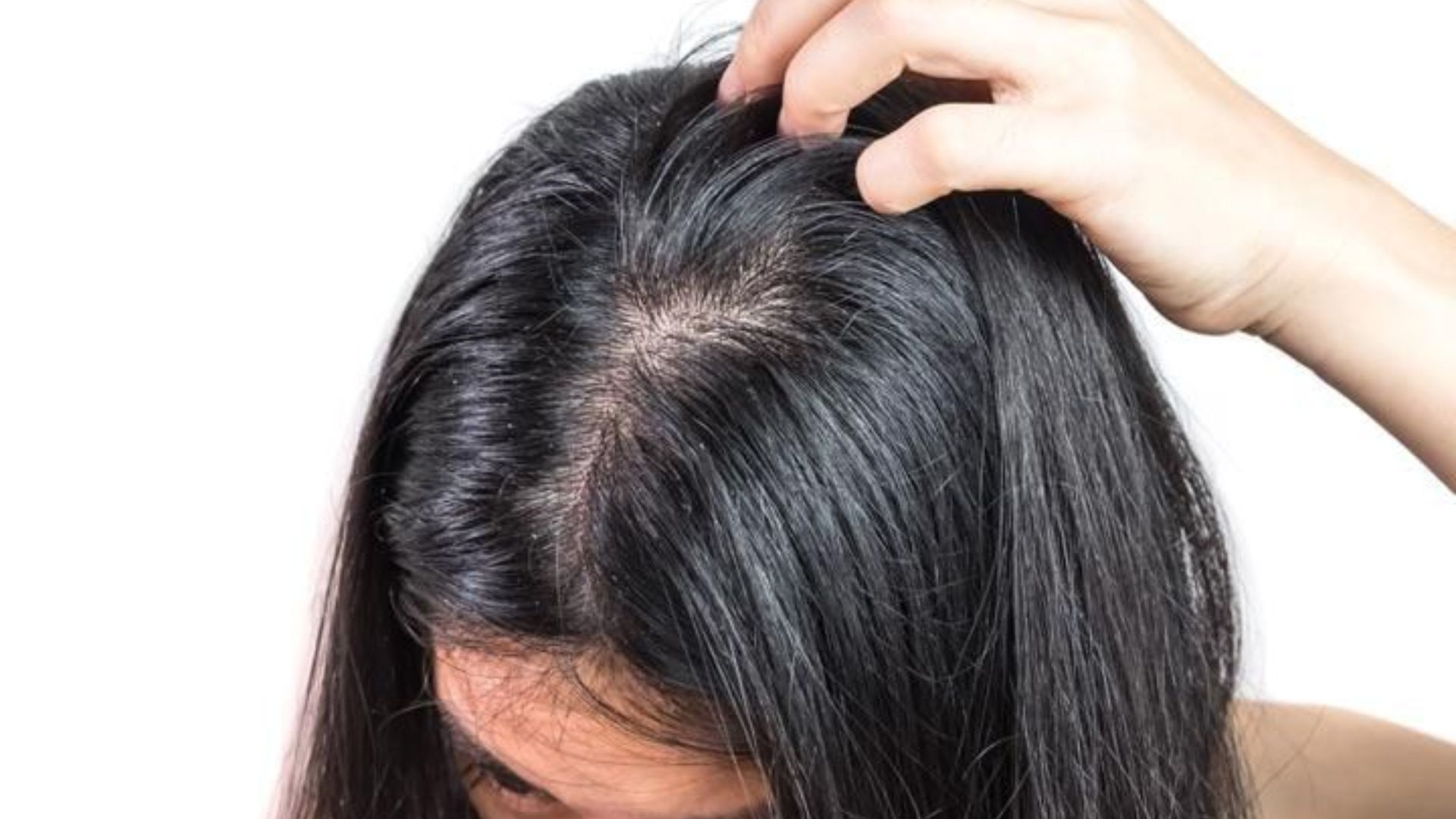 A woman is using a comb to style her hair, focusing on her reflection in a mirror.