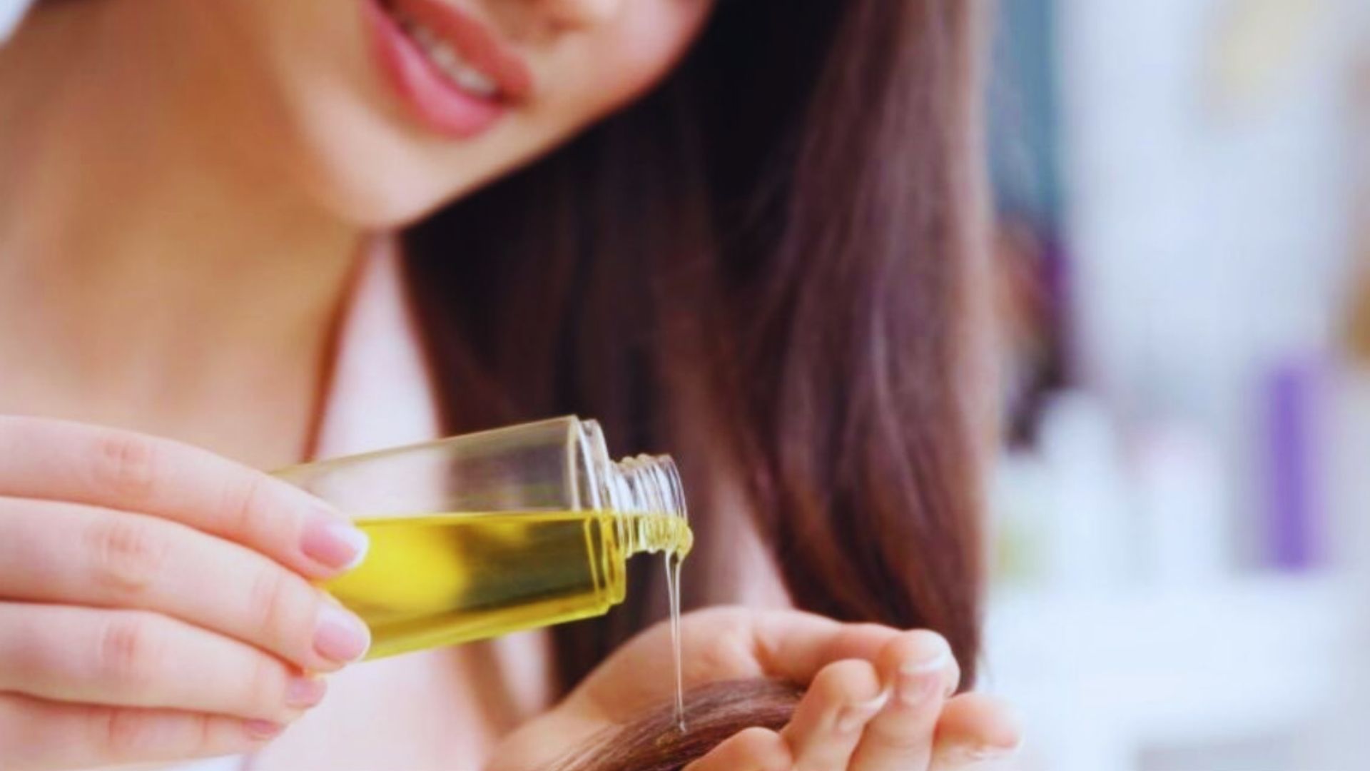 A woman applies castor oil to her hair, holding the bottle in one hand while gently massaging her scalp.