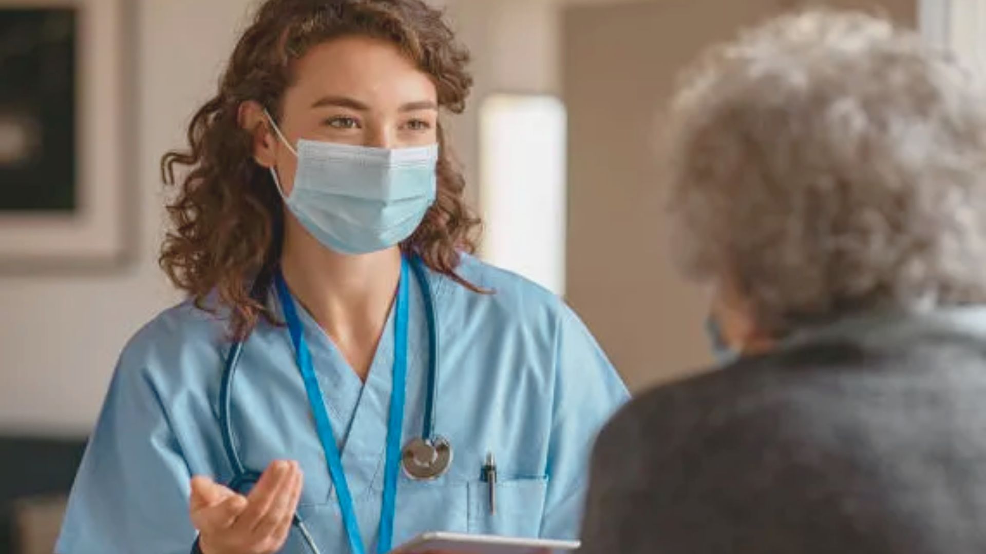 A nurse in a face mask converses with an older woman, discussing health information related to doxycycline treatment.