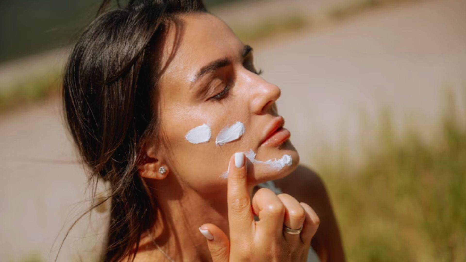 A woman applying sunscreen to her face, ensuring protection from the sun's harmful rays.