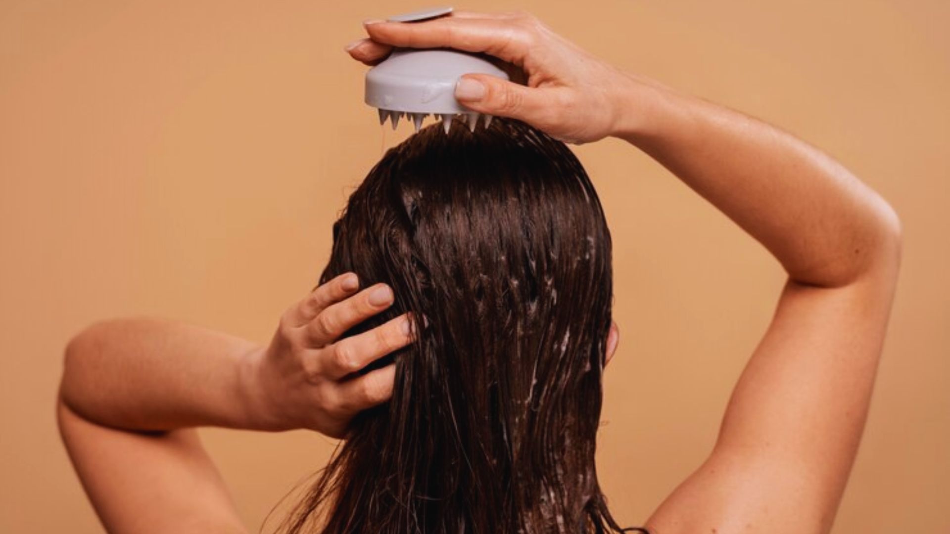 A woman is brushing her hair with a hairbrush, focusing on her reflection in a mirror.
