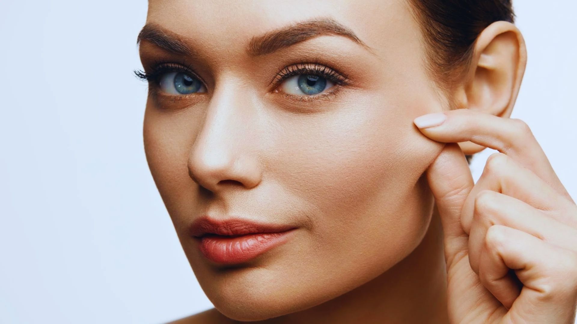 A woman with blue eyes gently touches her face, showcasing a moment of contemplation or self-reflection.