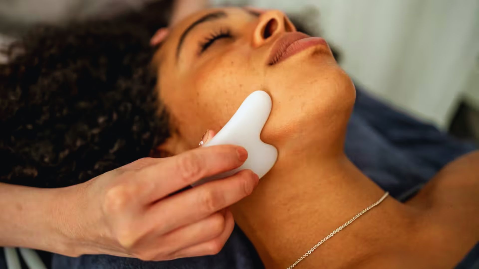 A woman receiving a facial treatment using a handheld device in a serene spa setting.