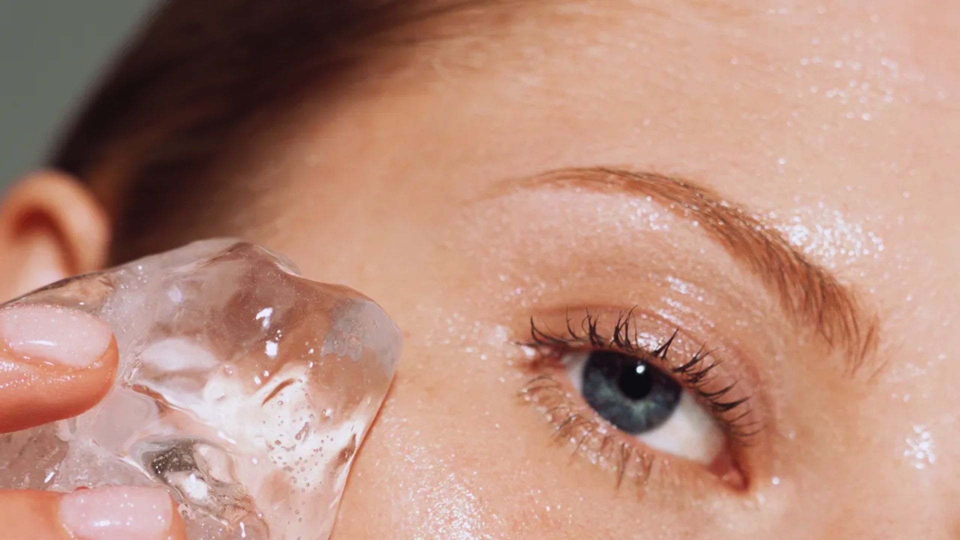 A woman holds a large ice cube, showcasing its size and clarity against a neutral background.
