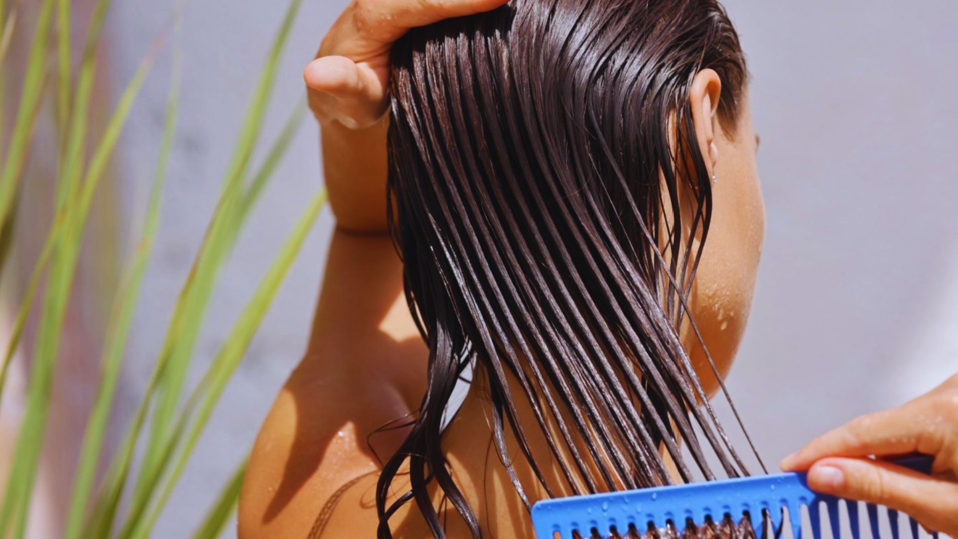 A woman is using a comb to style her hair, focusing on her reflection in a mirror.