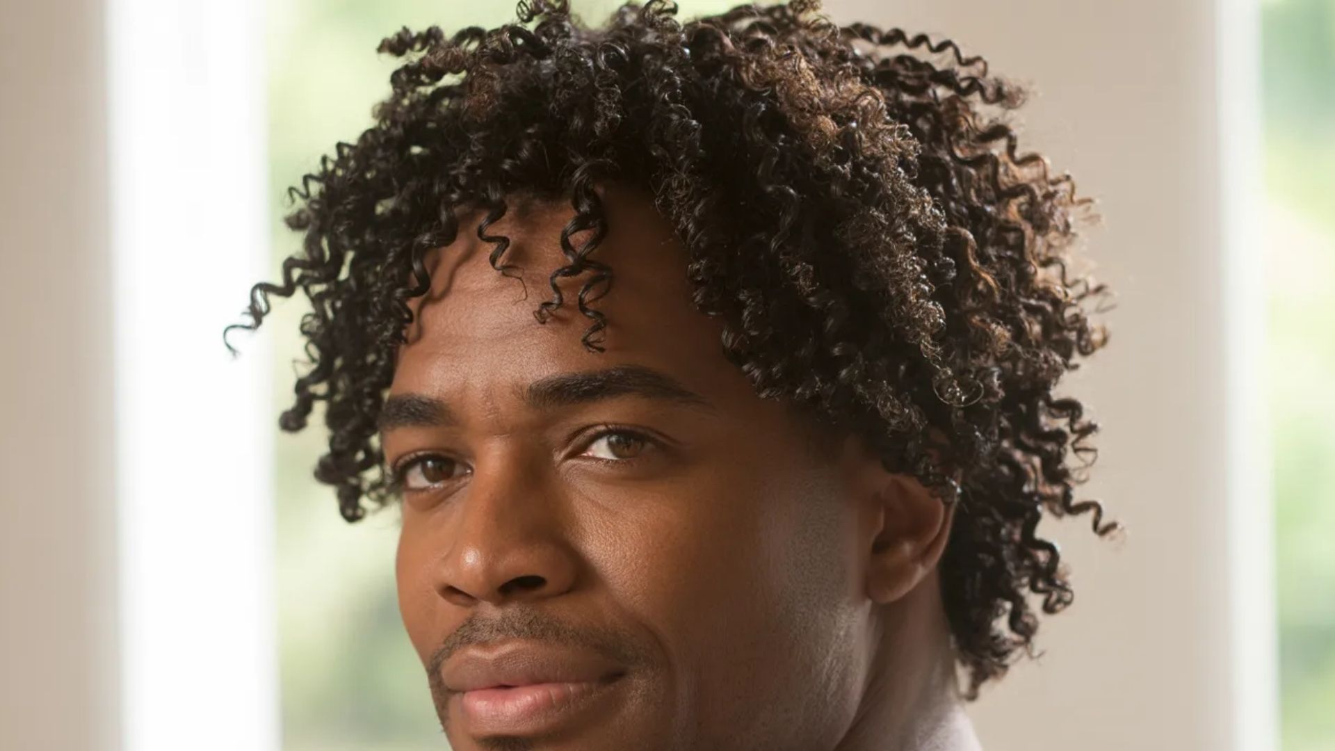 A man with curly hair gazes directly at the camera, showcasing a friendly expression.