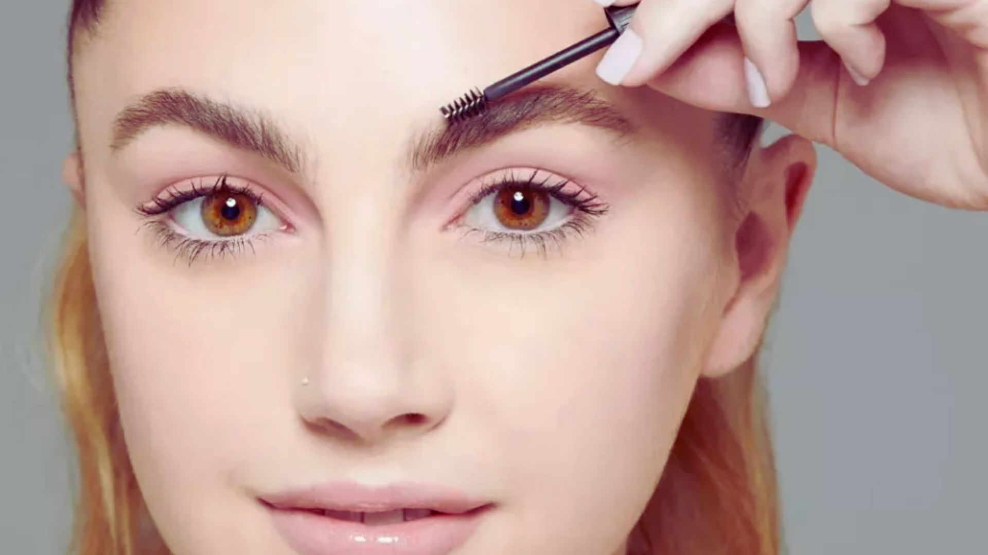 A woman carefully applies eyebrow makeup with a brush, focusing on achieving a precise and polished look.