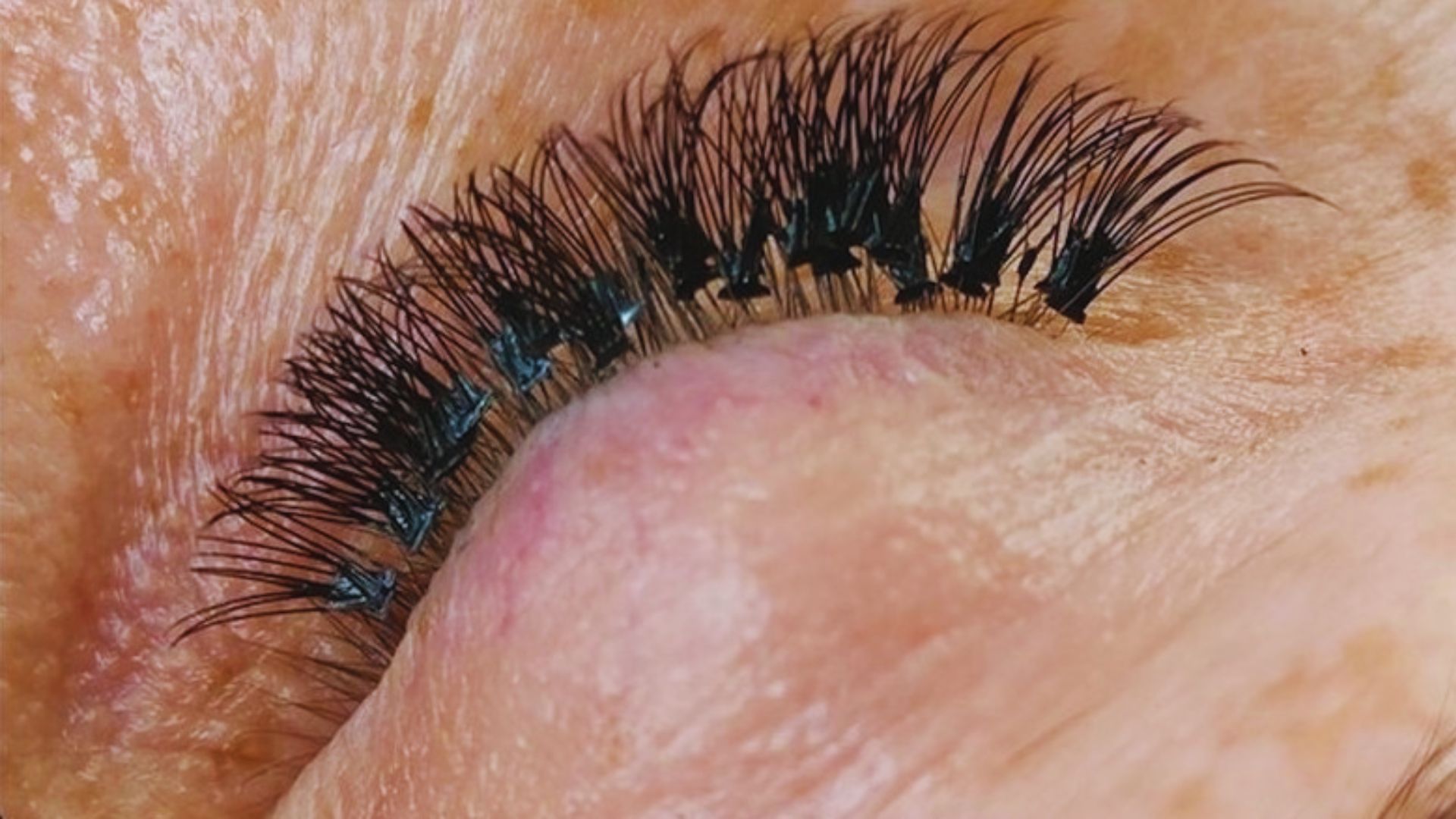 A close-up of a woman's eye showcasing long, elegant eyelashes against a soft background.