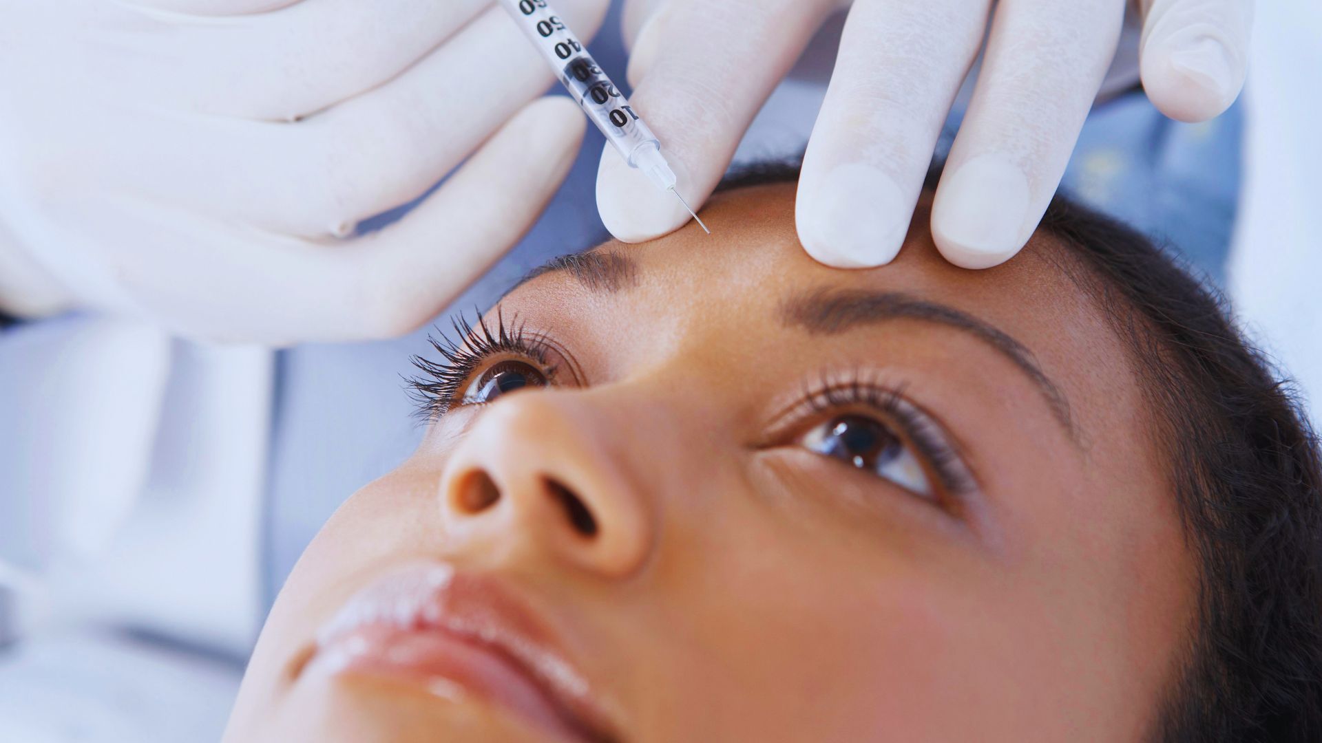 A woman receiving eyebrow shaping from a doctor in a clinical setting.
