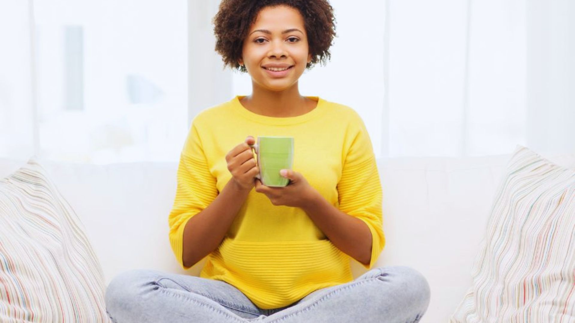 A woman sitting on a couch, holding a cup of coffee, appears relaxed and enjoying her beverage.
