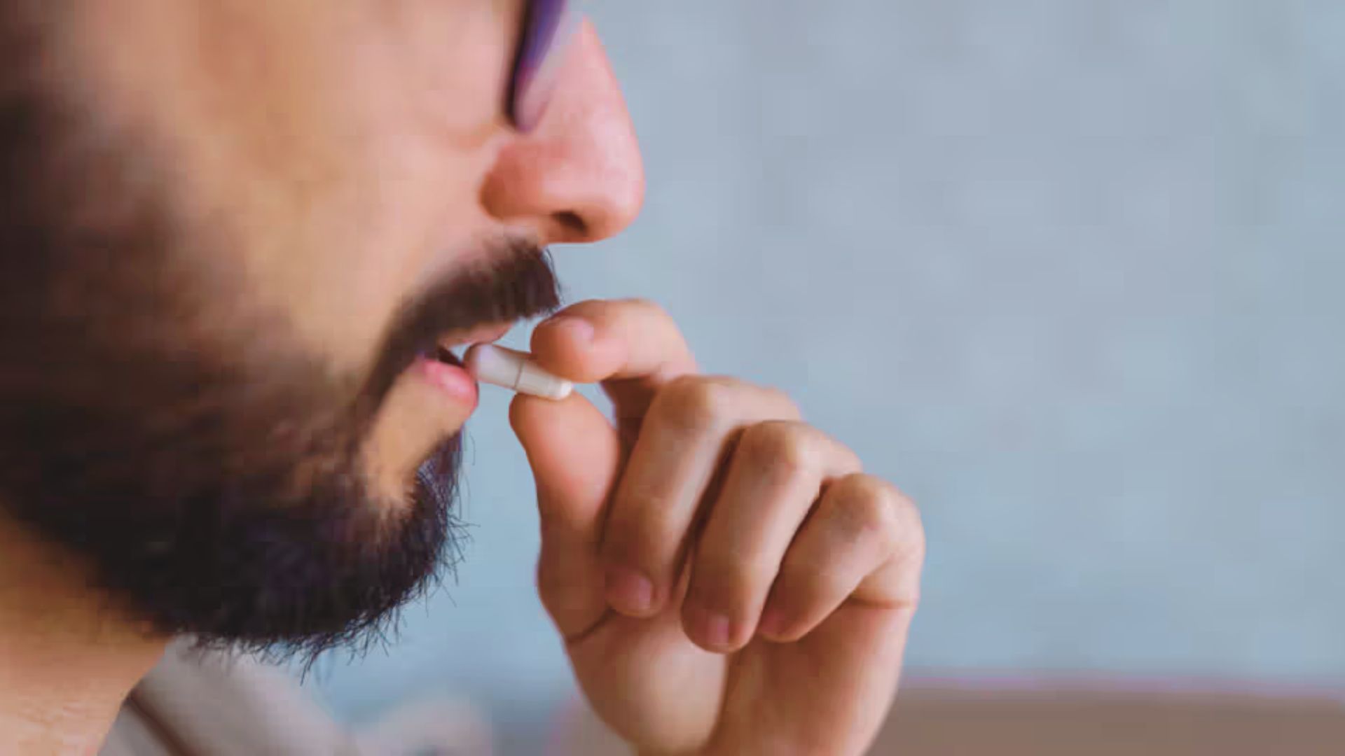 Bearded man with glasses holding a capsule related to acne treatment