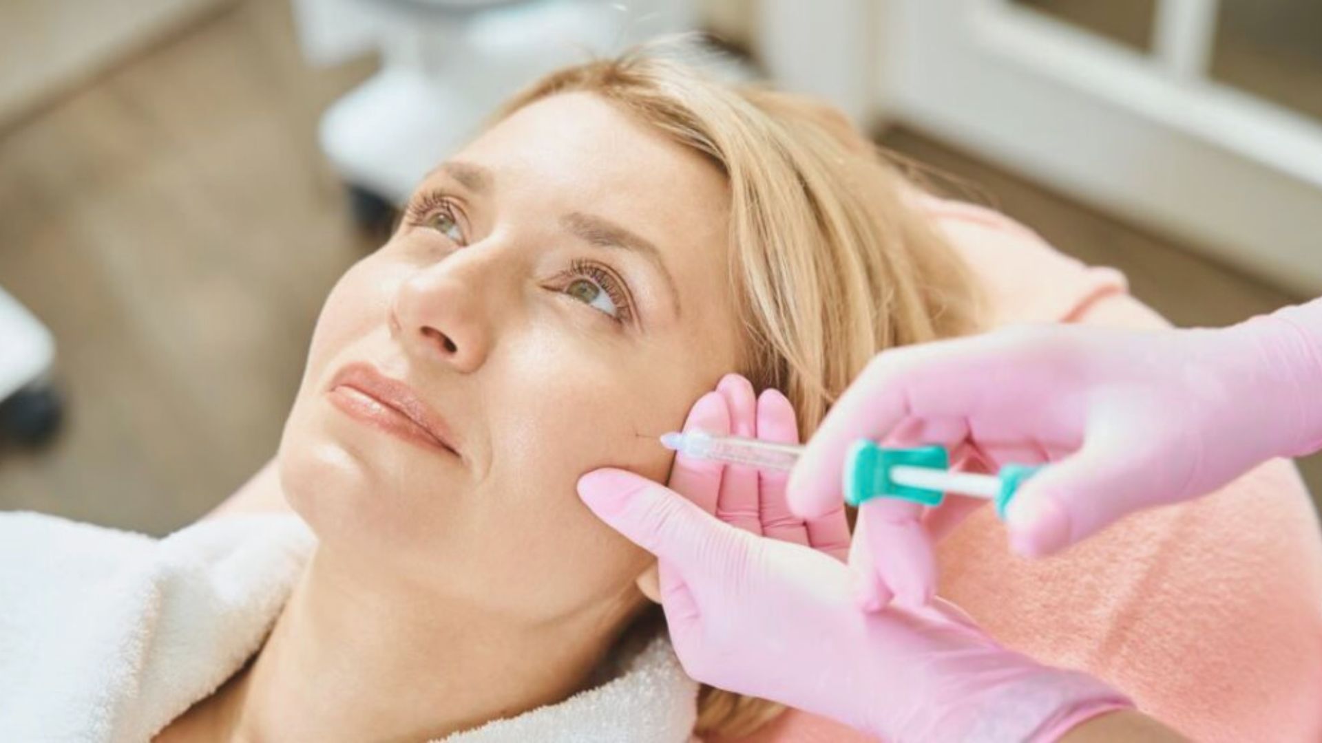 A woman receiving a facial injection in a clinical setting, focused on her face and the medical professional's hands.