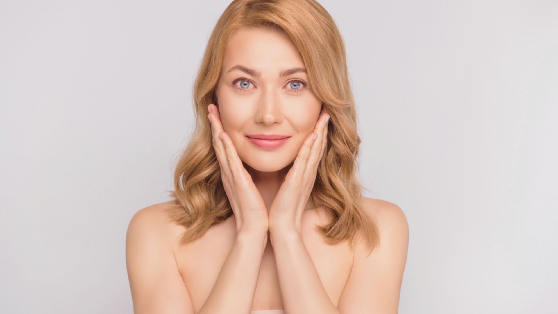 Beautiful woman with clear skin gently resting her hands on her face, showcasing a serene and natural expression.