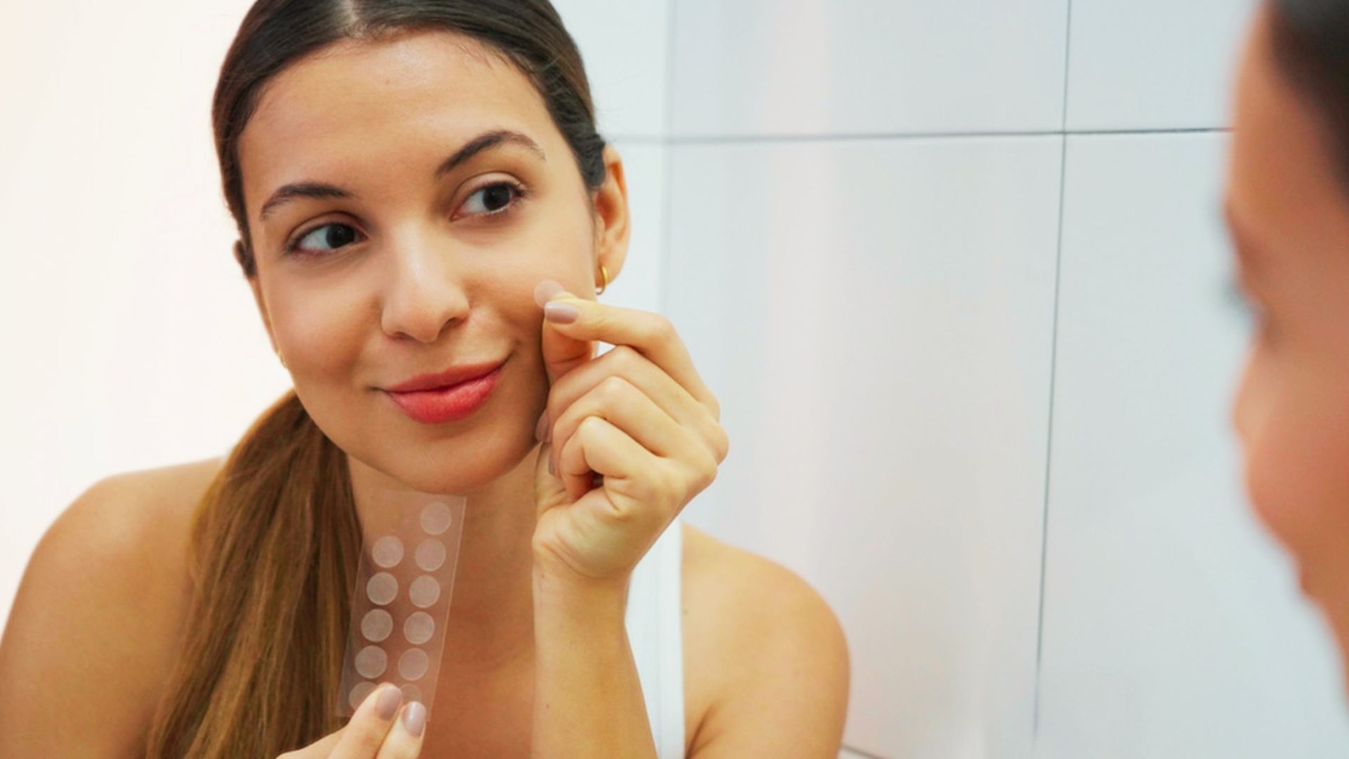 A woman applies a pimple patch sticker to her face, focusing on skincare and blemish treatment.