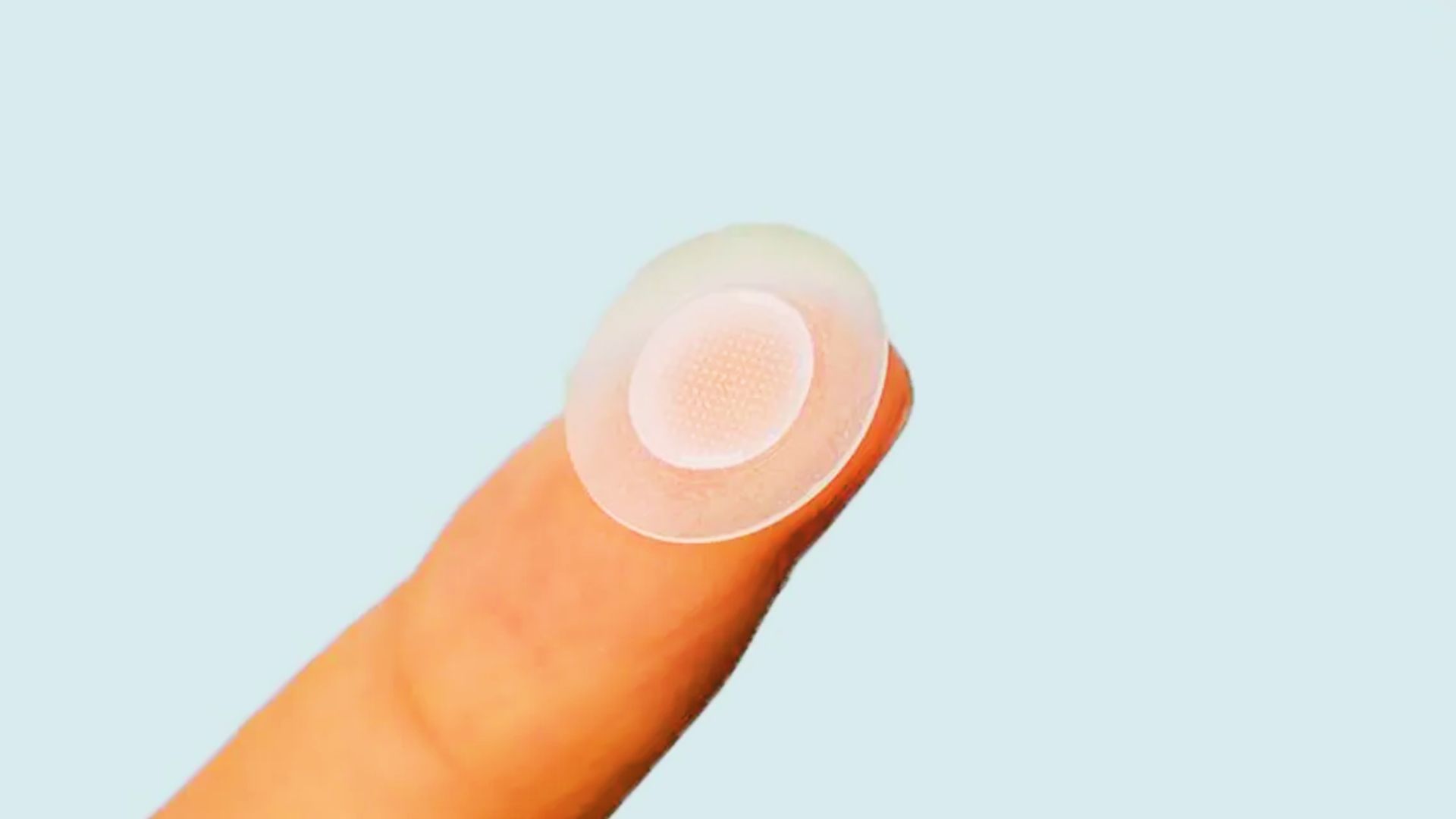 A person holding a small white pimple patch button on their fingertip, showcasing its size and design.
