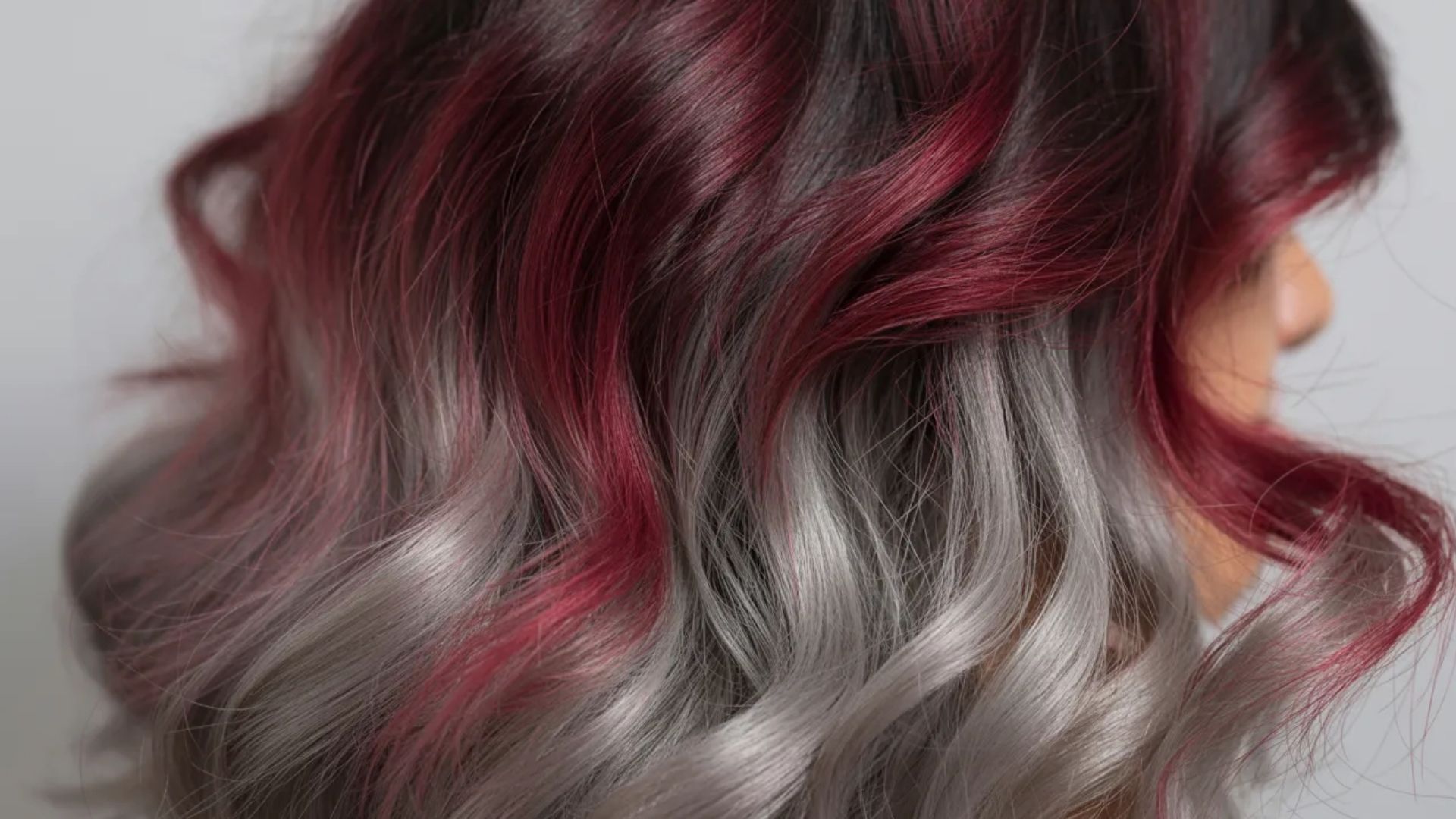 . The image features a woman with a blend of red and grey hair, highlighting her distinctive and colorful appearance.