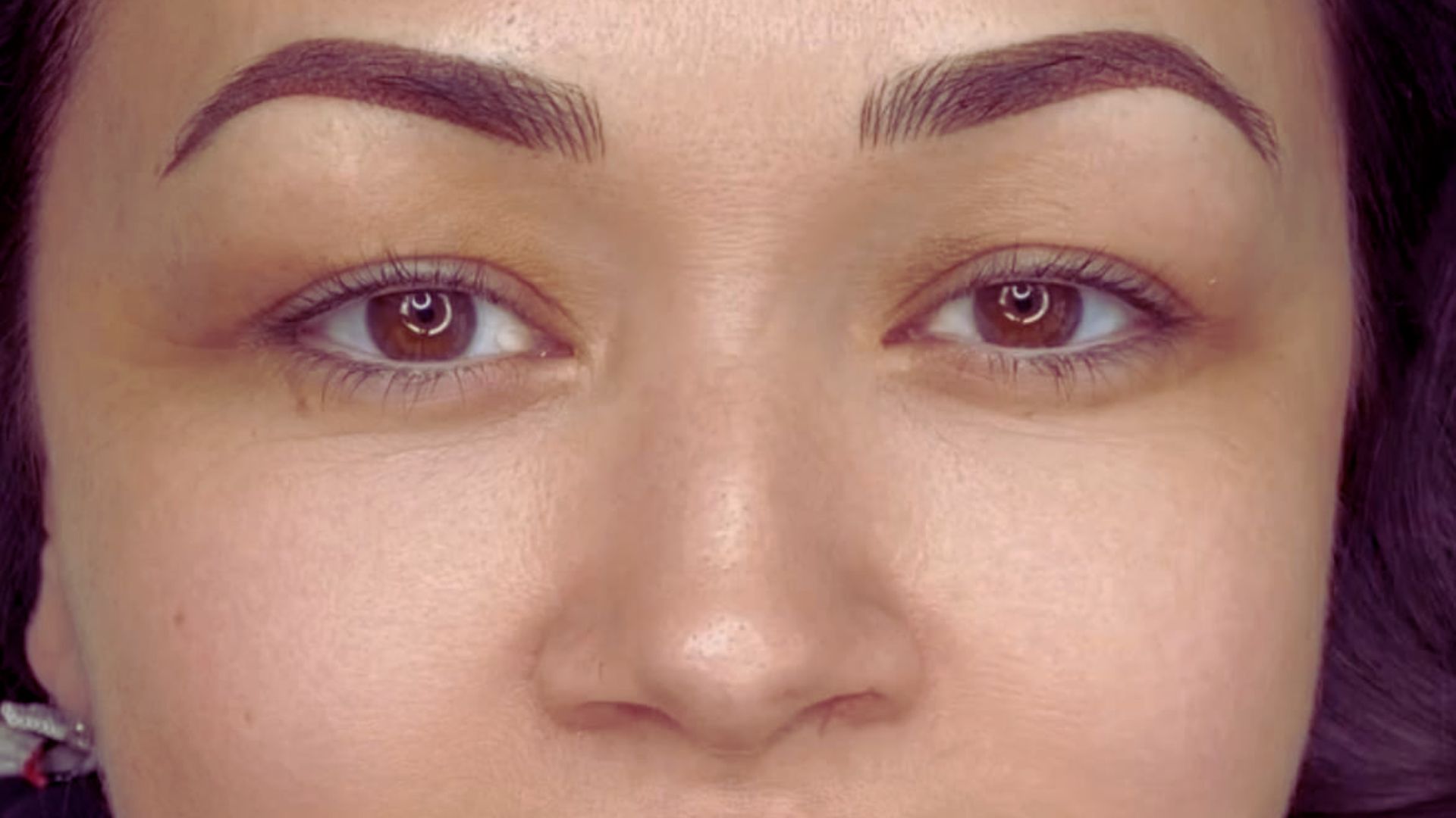 A woman with brown eyes and a prominent nose, looking directly at the camera with a neutral expression.