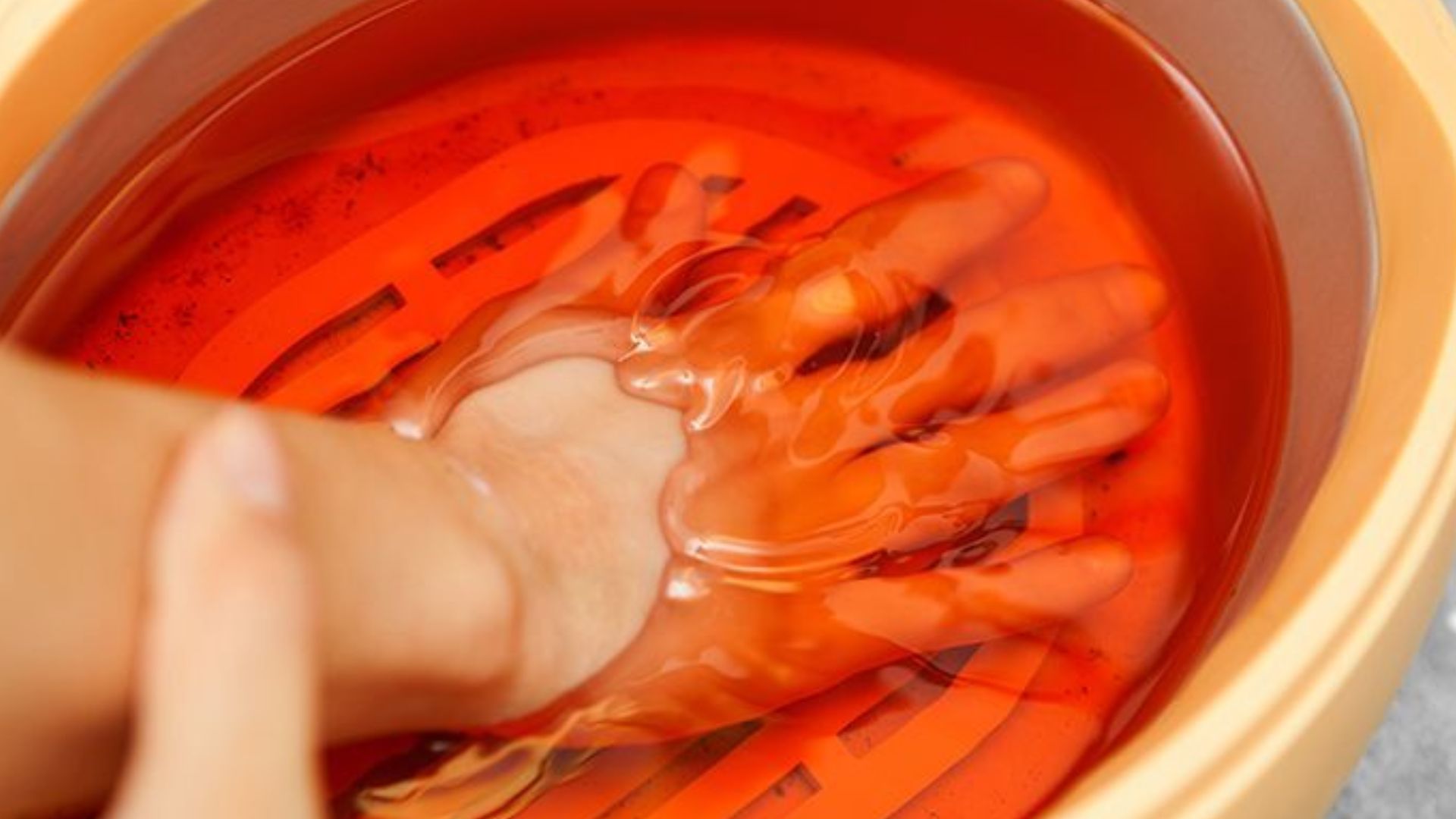 A hand submerged in a bowl filled with bright red liquid, suggesting a vibrant and possibly messy activity.