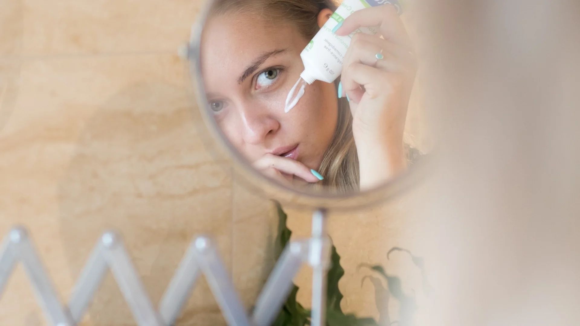 A woman applies eye cream while looking in the mirror, focusing on her skincare routine and active ingredient adjustments.