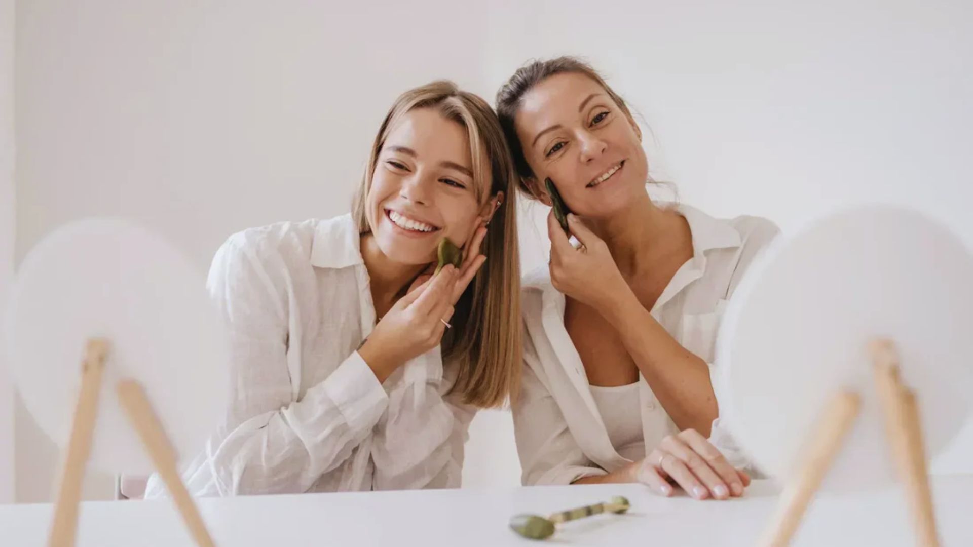 Two women smiling at their reflections in a mirror, enjoying a moment of connection and self-appreciation.