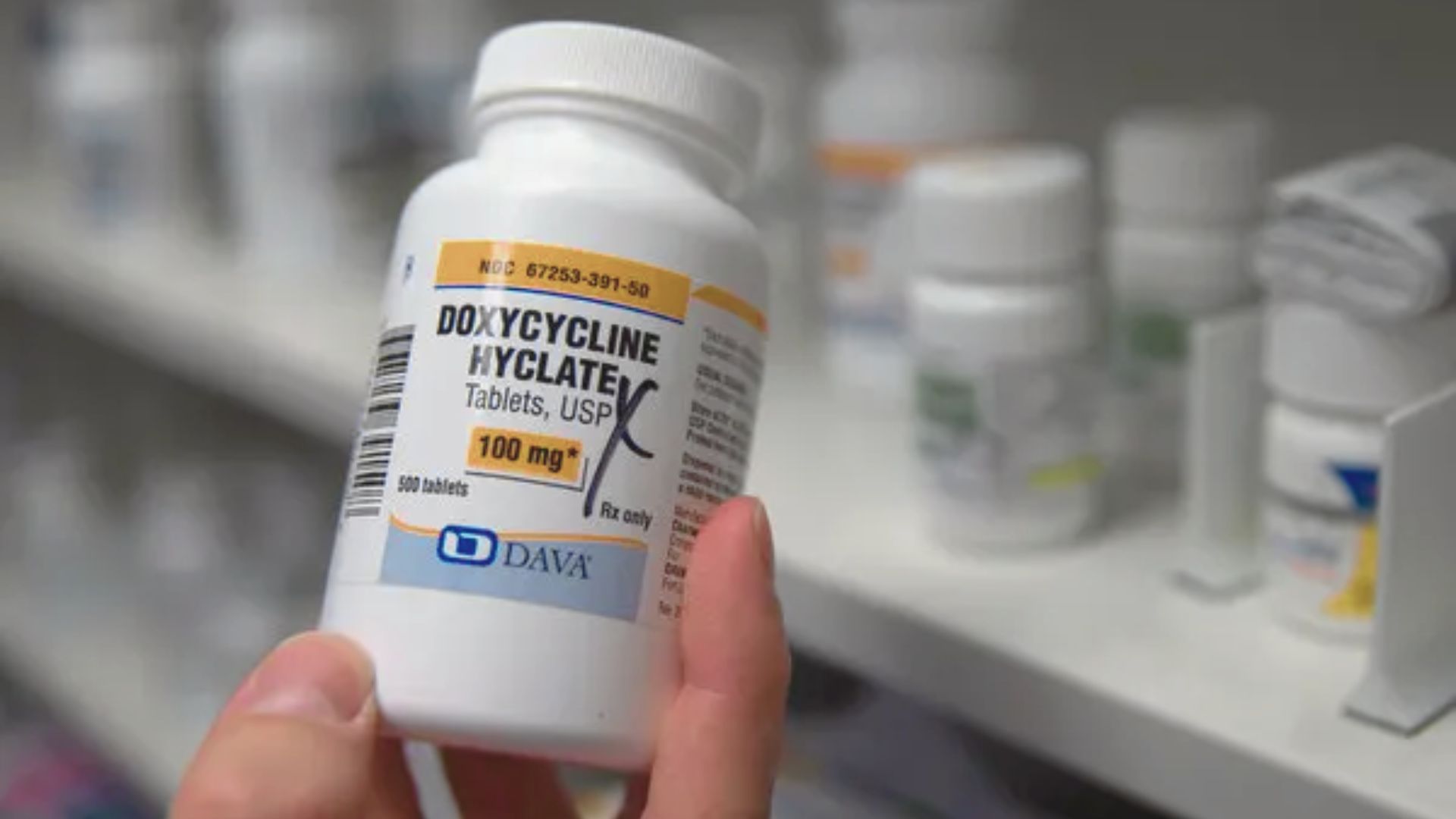 A pharmacy employee displays a bottle of doxycycline, a prescription pain medication