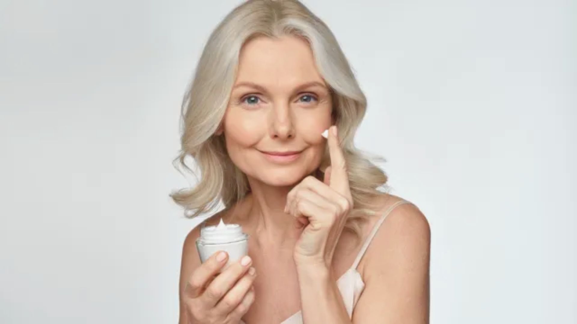 A woman smiling while holding a jar of cream in her hand.