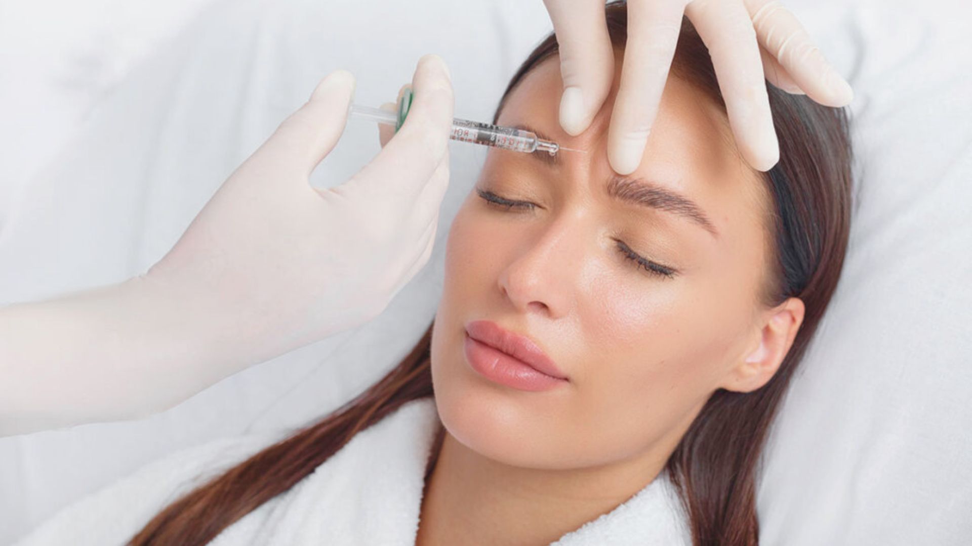 A woman receiving a facial injection in a clinical setting, focused on her face and the medical professional administering it.