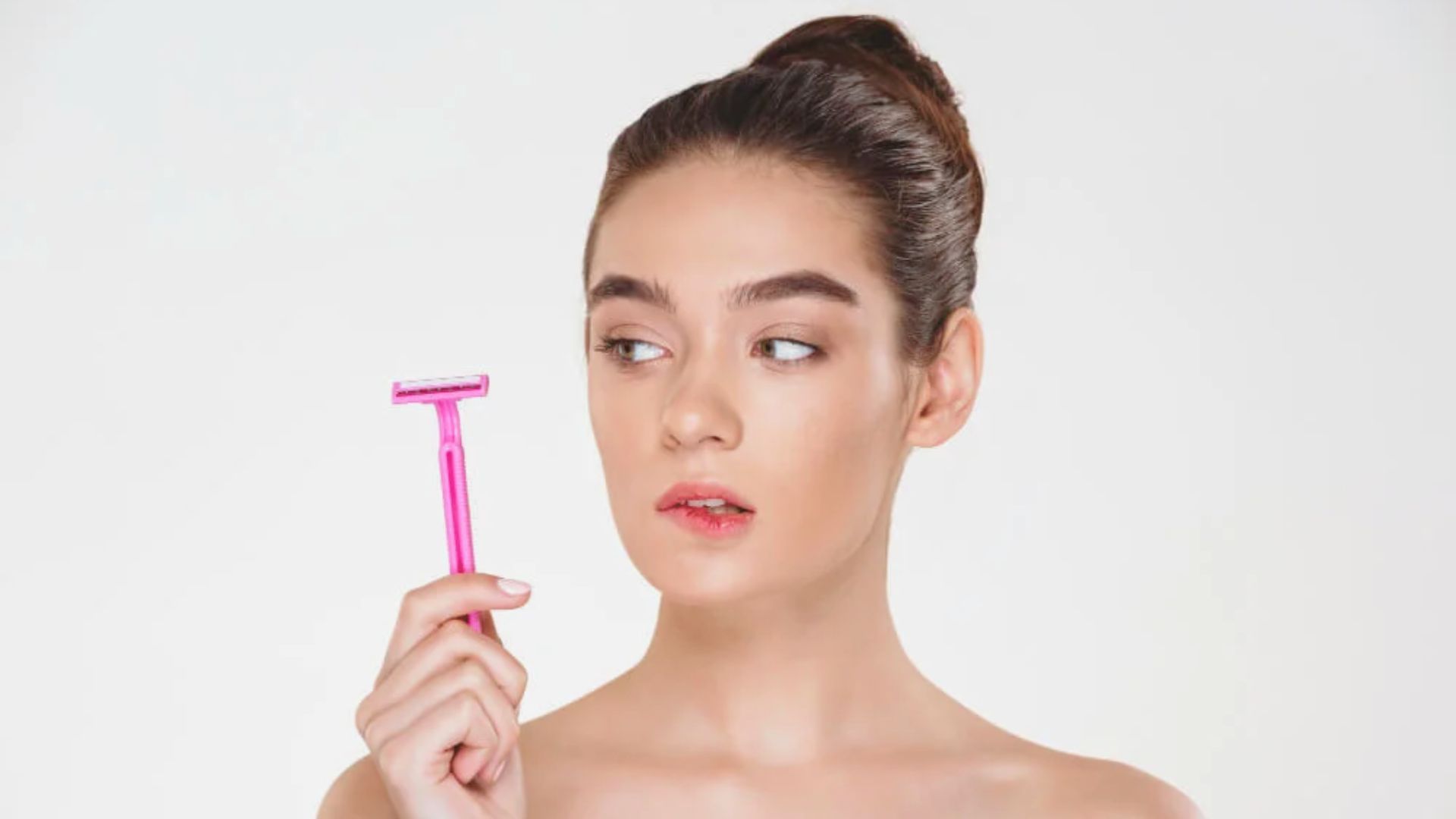 A woman holds a pink razor in her hand, ready for personal grooming.