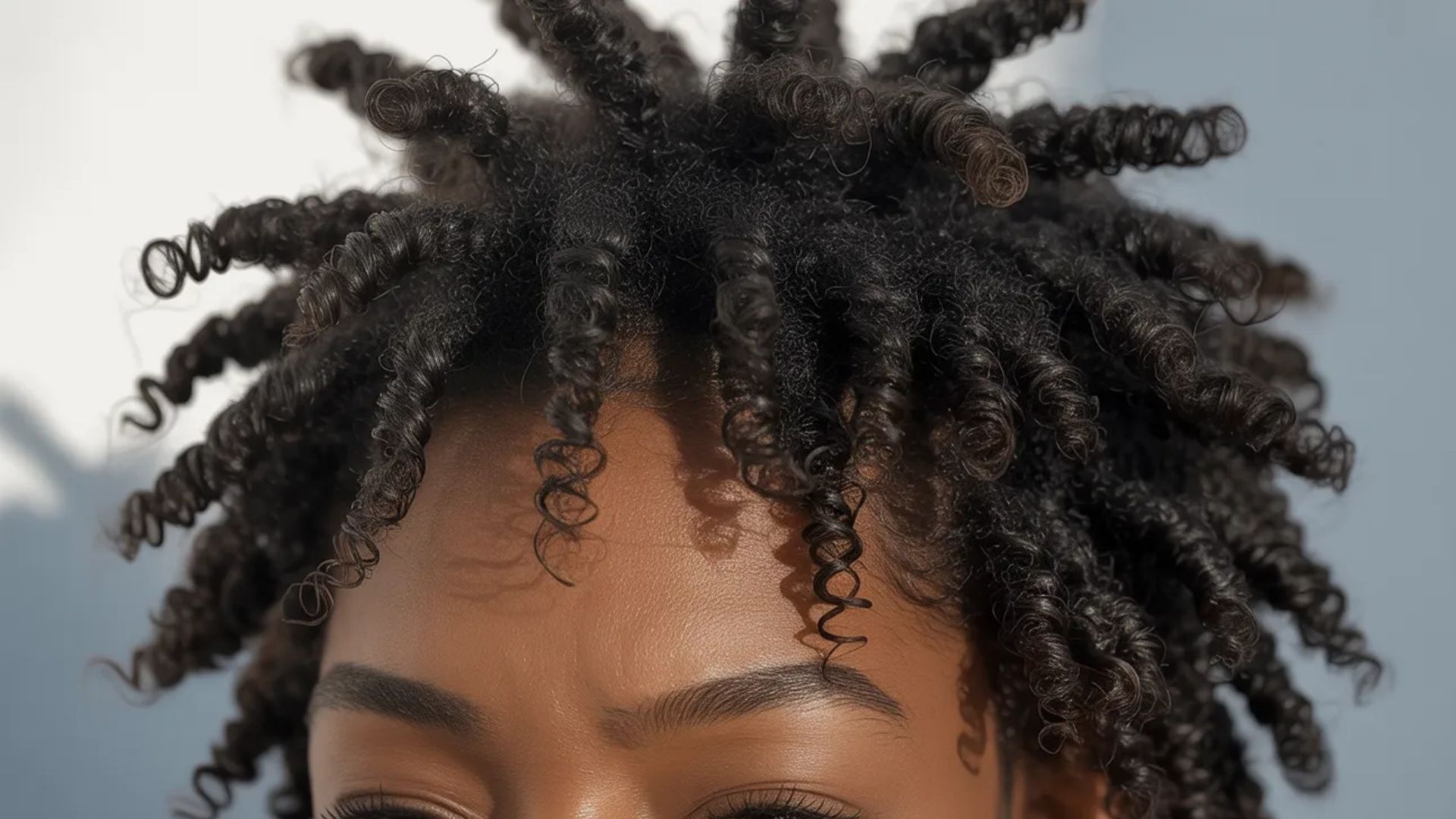 A woman with curly hair gazes downward, her expression thoughtful and introspective.