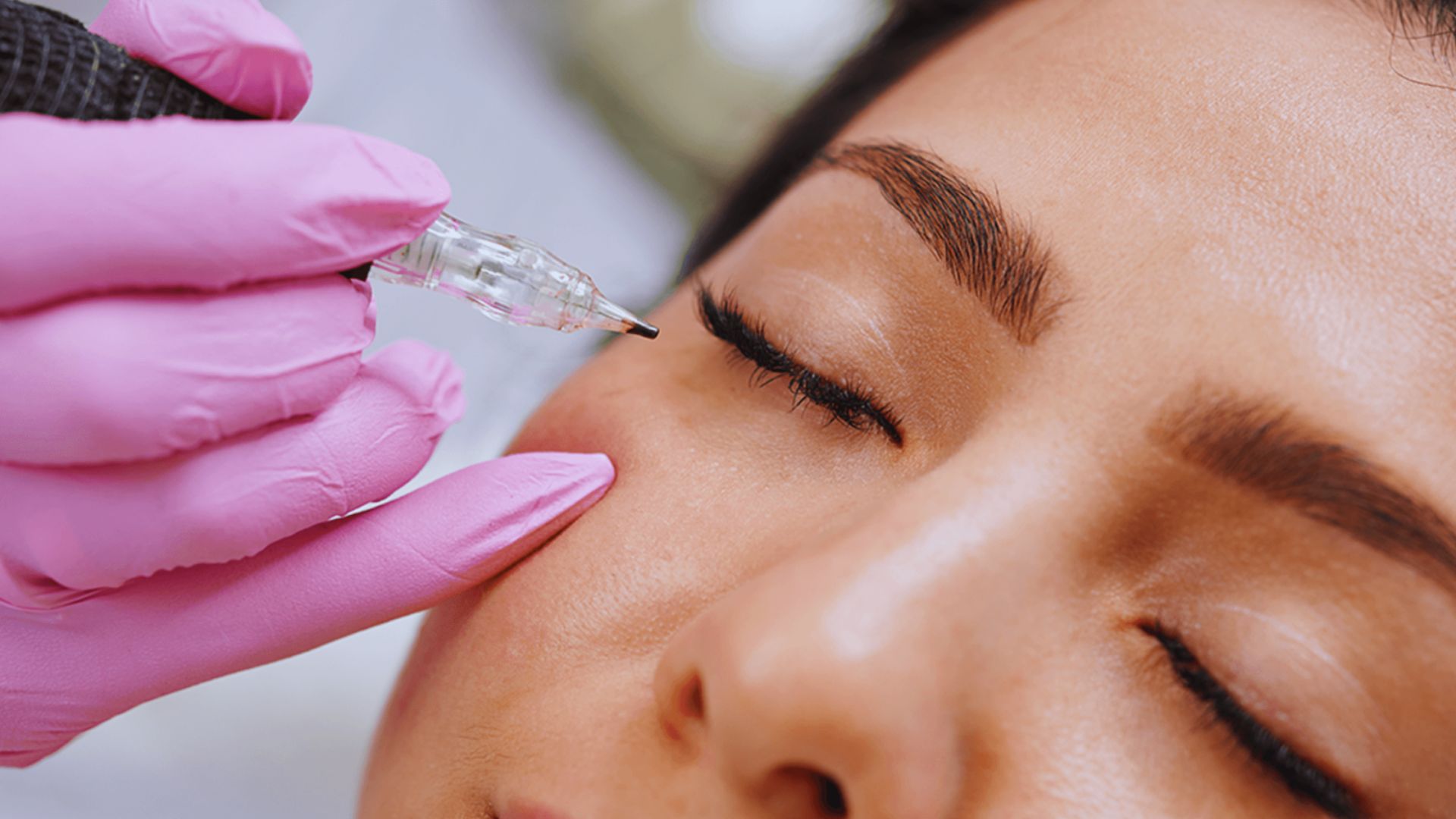 A woman undergoing eyebrow shaping with a needle, focused on her treatment in a salon.