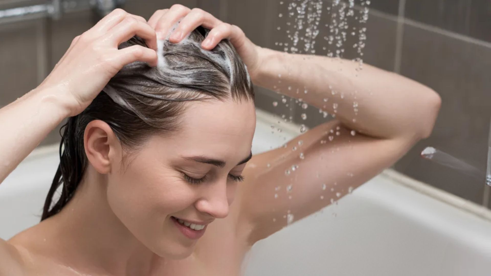 A woman is in a bathtub, lathering her hair with shampoo, creating a relaxing atmosphere.